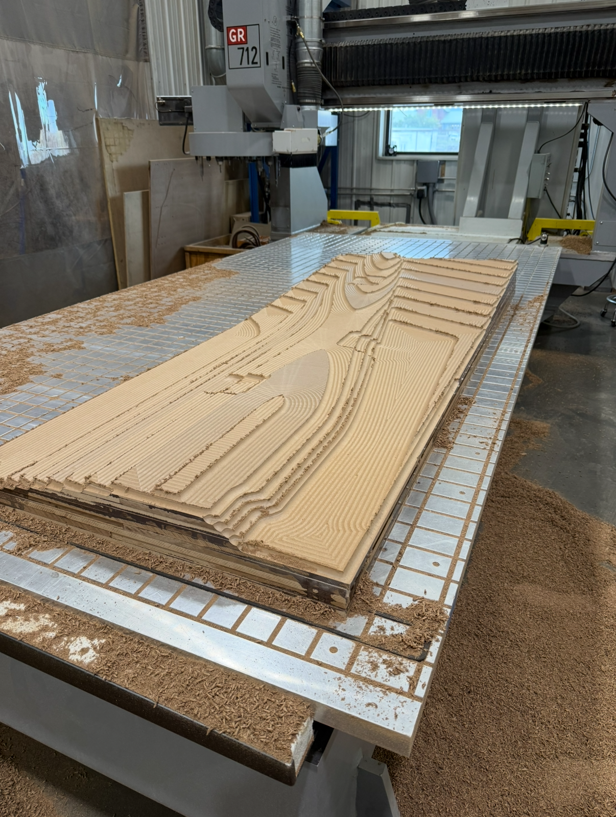 CNC machine carving a layered wooden art piece with intricate patterns in a woodworking workshop.