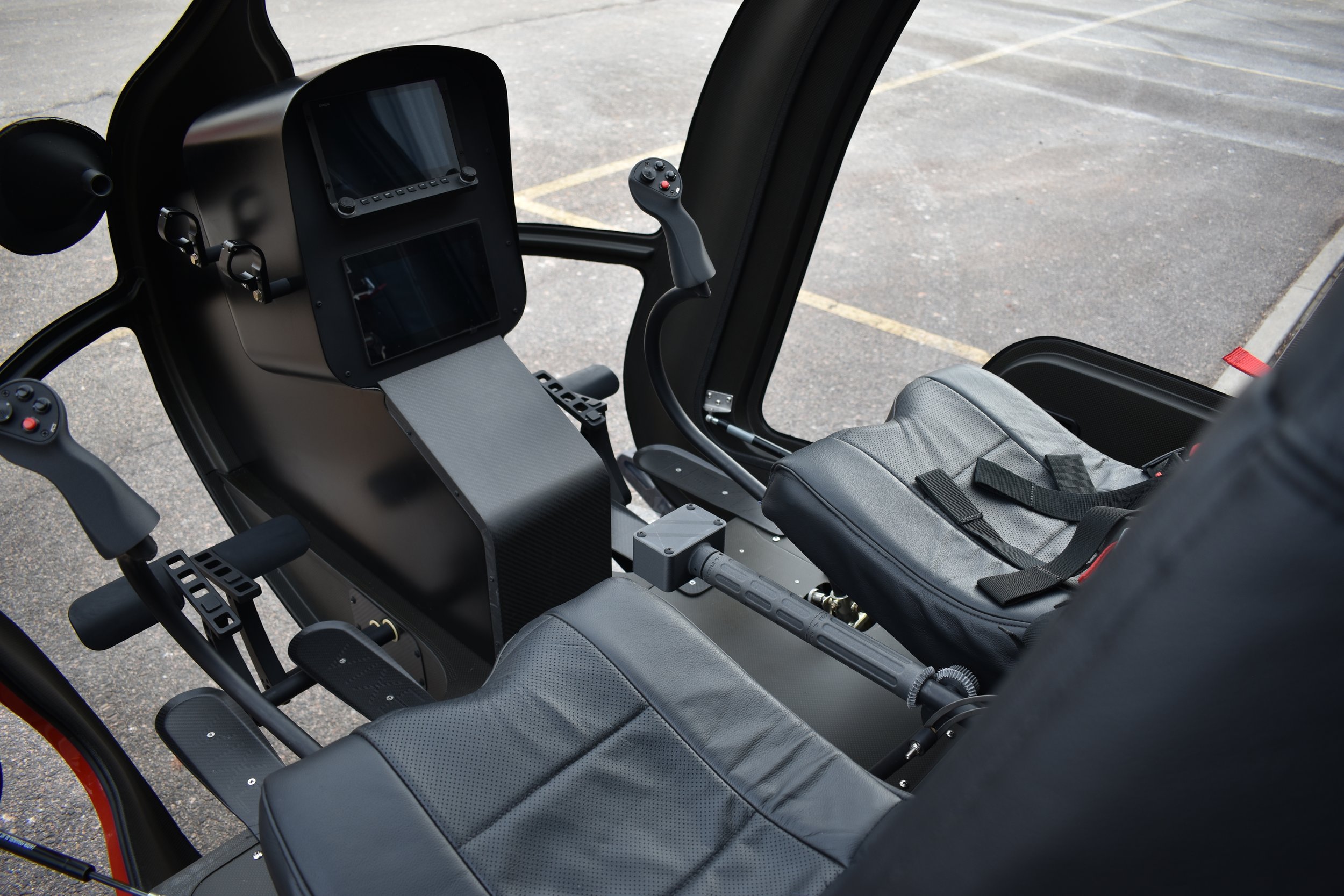 Interior of a helicopter cockpit with control sticks, a display screen, and seats.