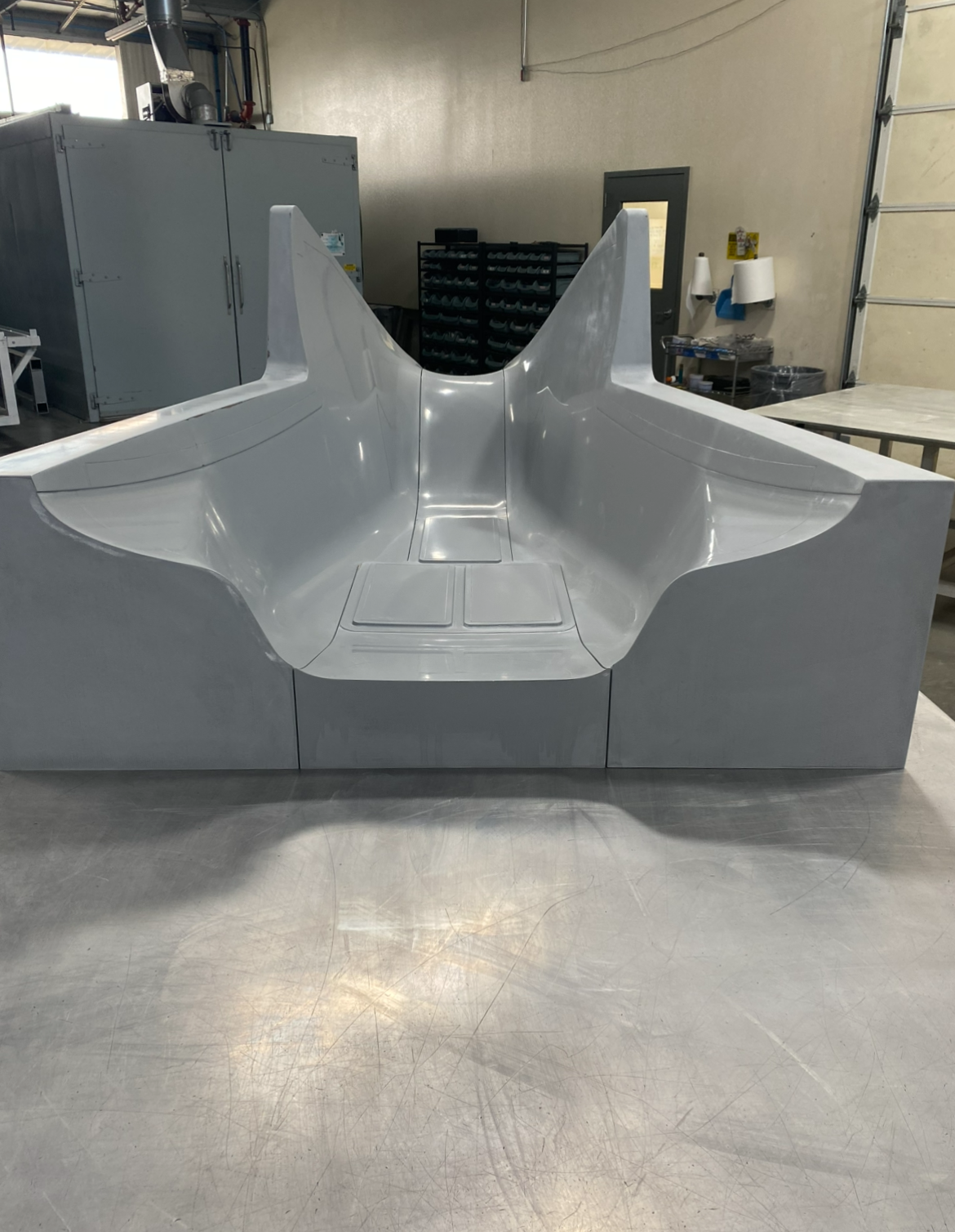 A metallic, streamlined vehicle cockpit or nose cone, likely for an aircraft or spacecraft, situated on a worktable in a workshop.