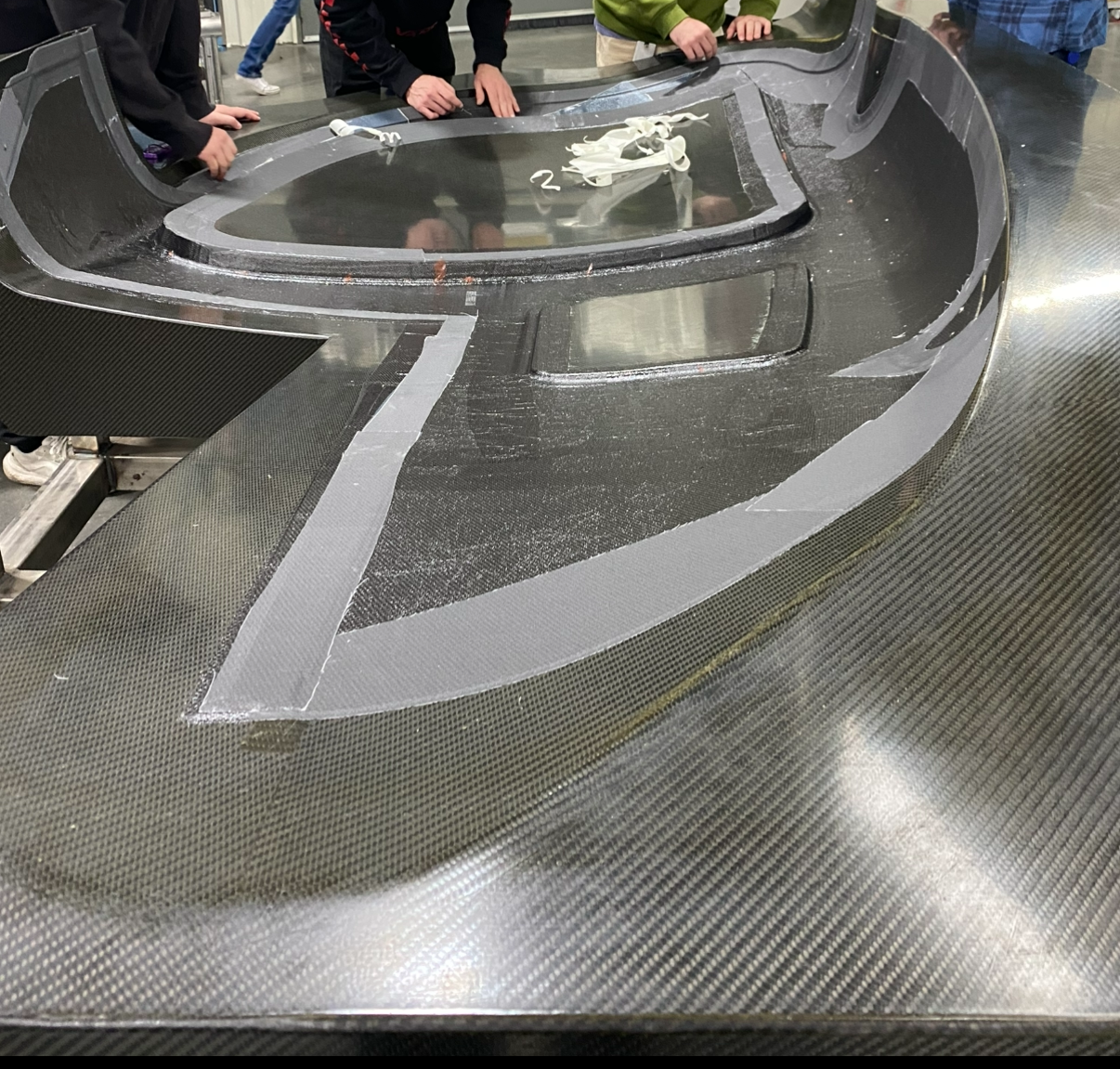 Close-up of a carbon fiber surface with a partially covered outlined shape. 