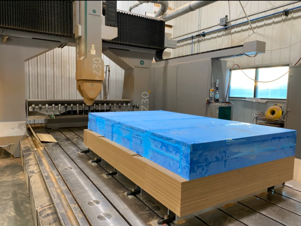 Large CNC machine with blue blocks and wooden base in an industrial workshop.