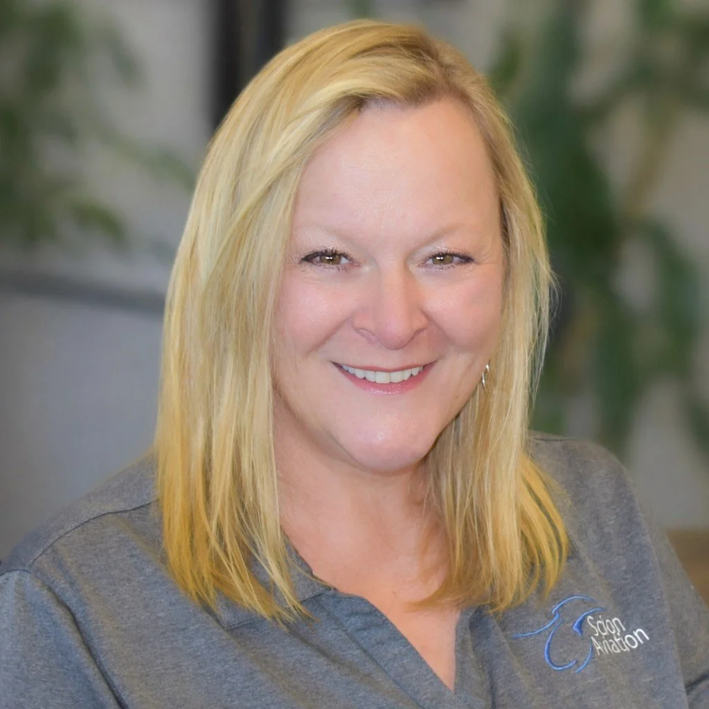 A smiling woman with blonde hair in a gray polo shirt with a logo that says Sun Airdon.