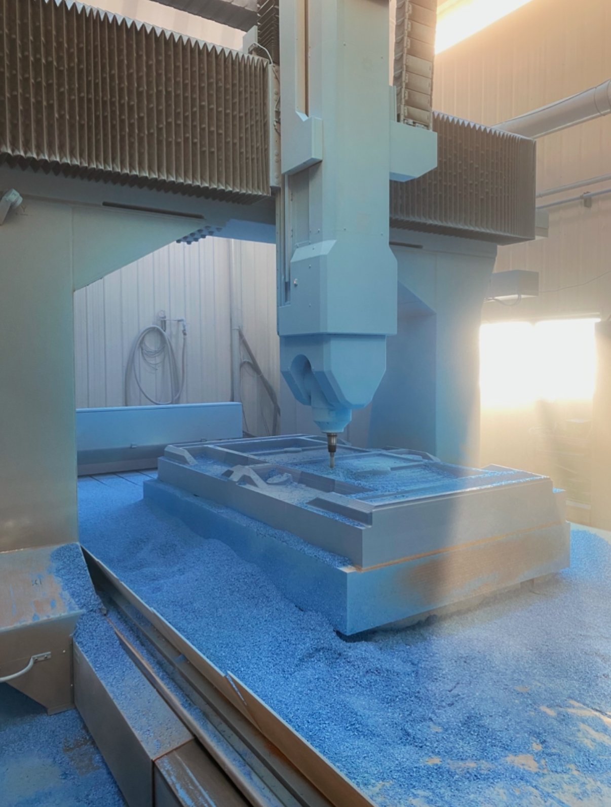 CNC machine processing metal in a workshop with bright sunlight streaming through a window.