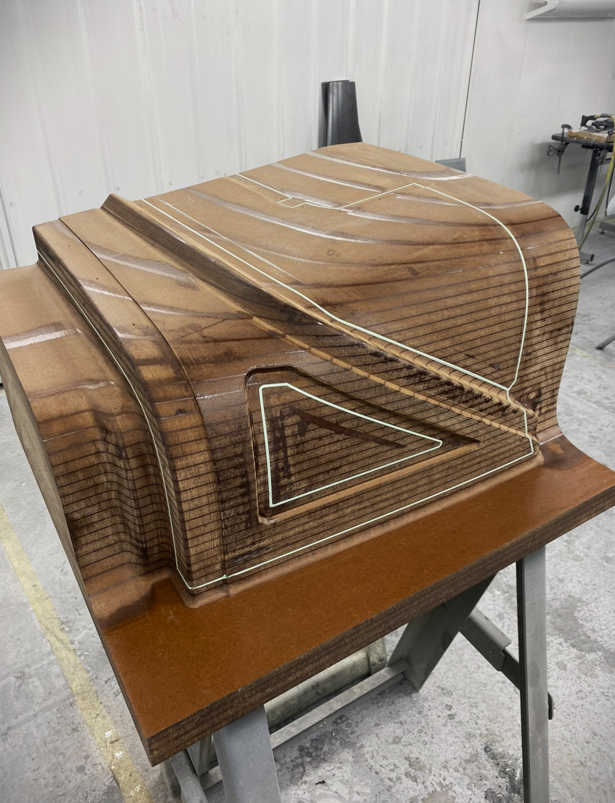 A wooden sculpture in progress, with visible wood grain and white lines mark on its surface, placed on a worktable in a workshop.