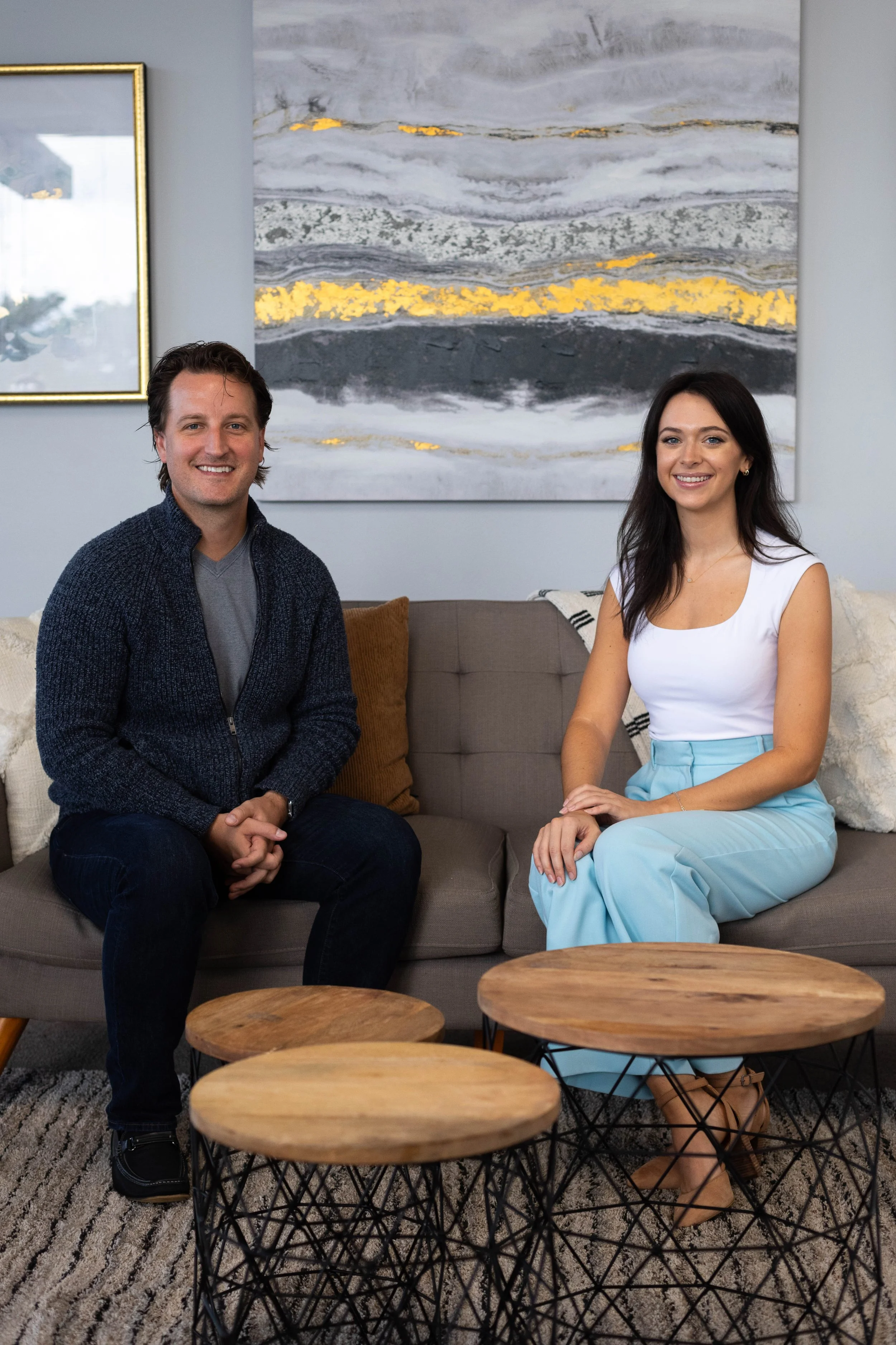 A man and woman are sitting on a sofa in the office of the Florida Relationship Institute, smiling at the camera, with abstract artwork hanging on the wall behind them.