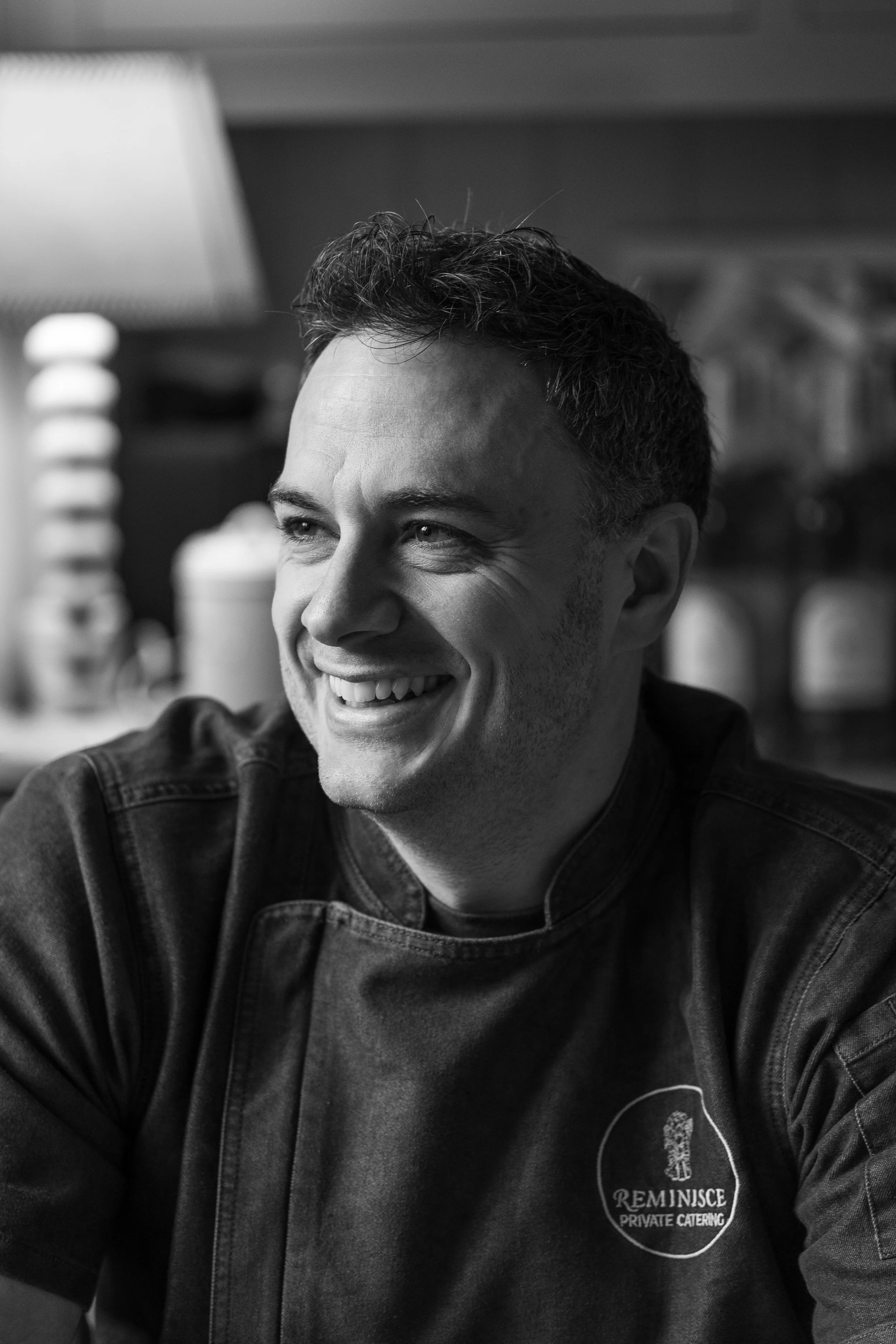 A smiling man in a chef's jacket with a logo that reads 'Reminisce Private Catering'.