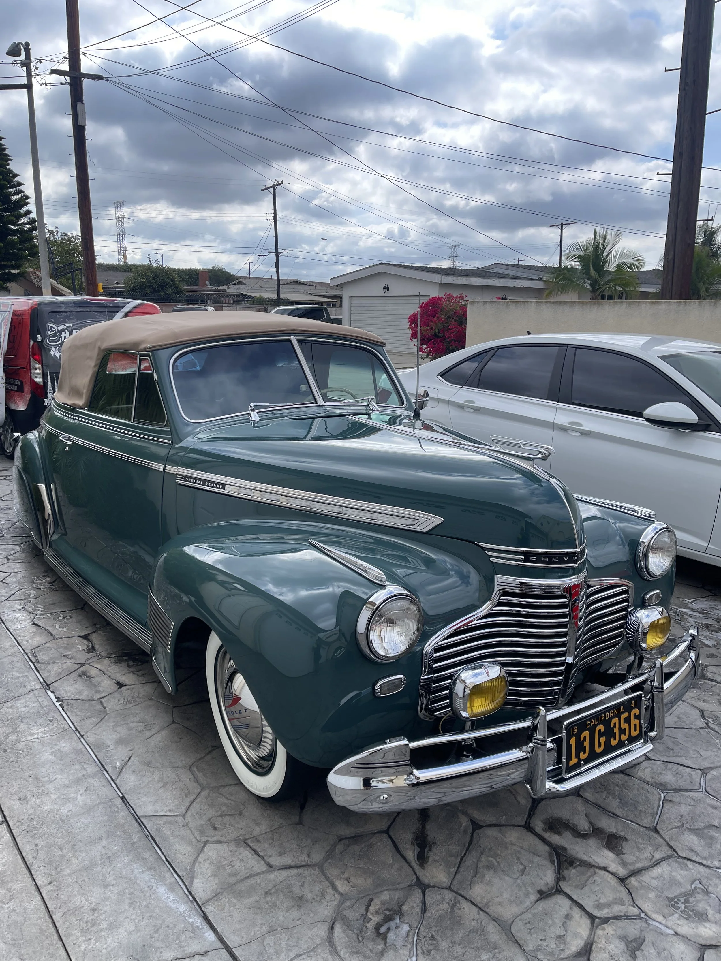 Green classic Chevrolet convertible from the 1940s parked in a driveway with chrome details and whitewall tires