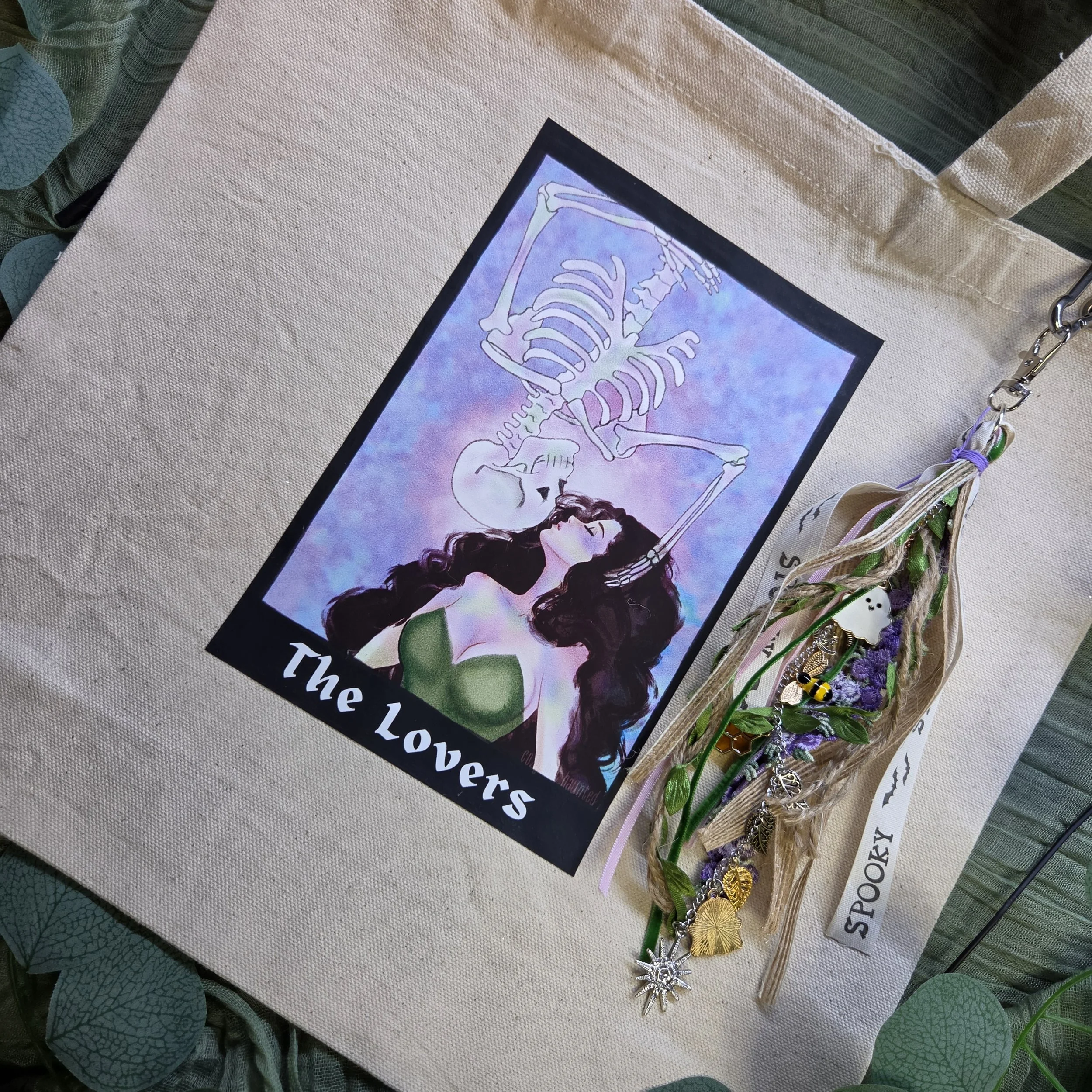 canvas tote bag with a tarot-style drawing of a woman kissing an upside-down skeleton descending toward her with a unique charm.