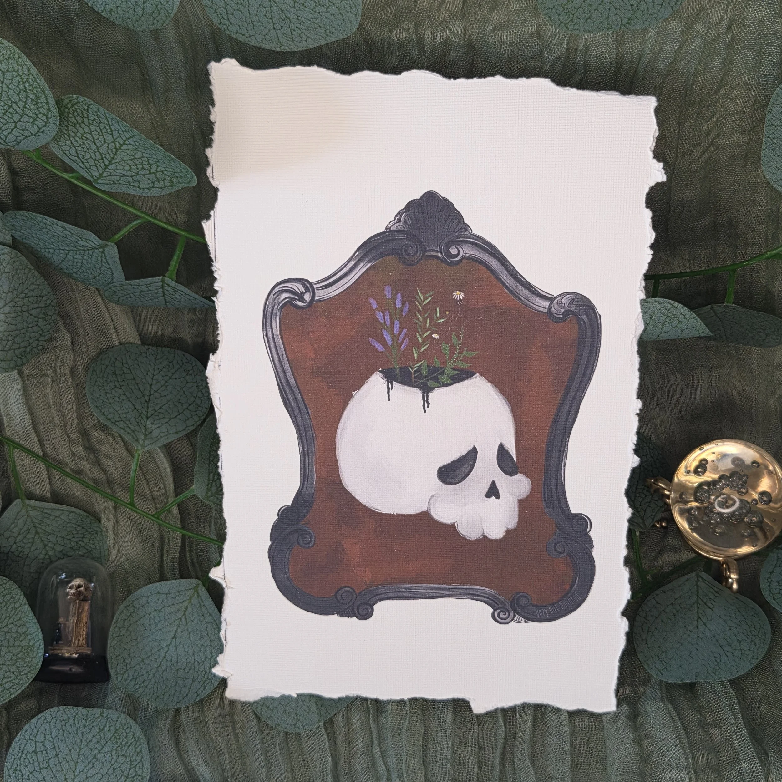 Drawing of a white skull framed by a red ornate background with small green plant elements on linen textured card stock with deckled edging.