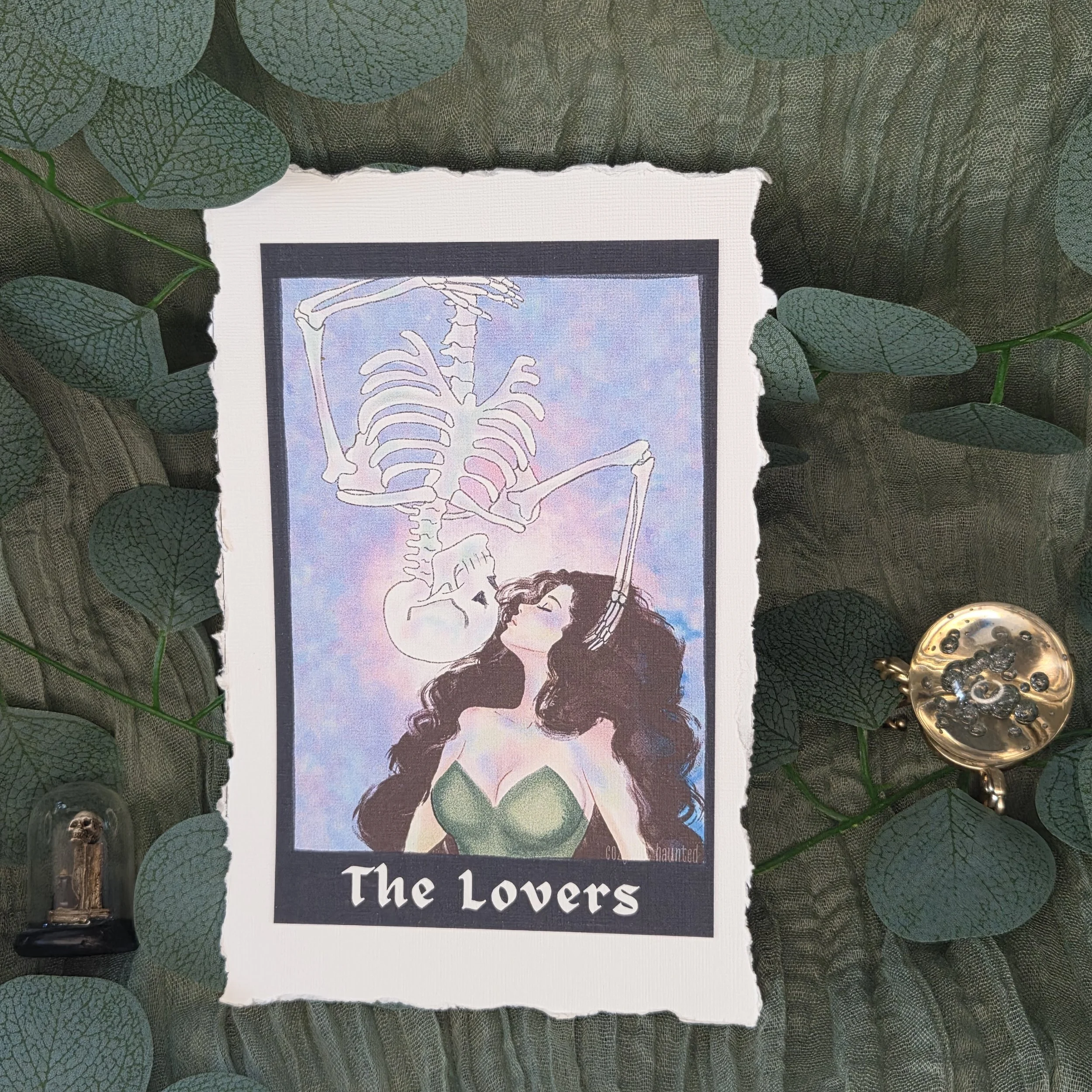 A tarot-style drawing of a woman kissing an upside-down skeleton descending toward her on lined textured card stock with deckled edging.