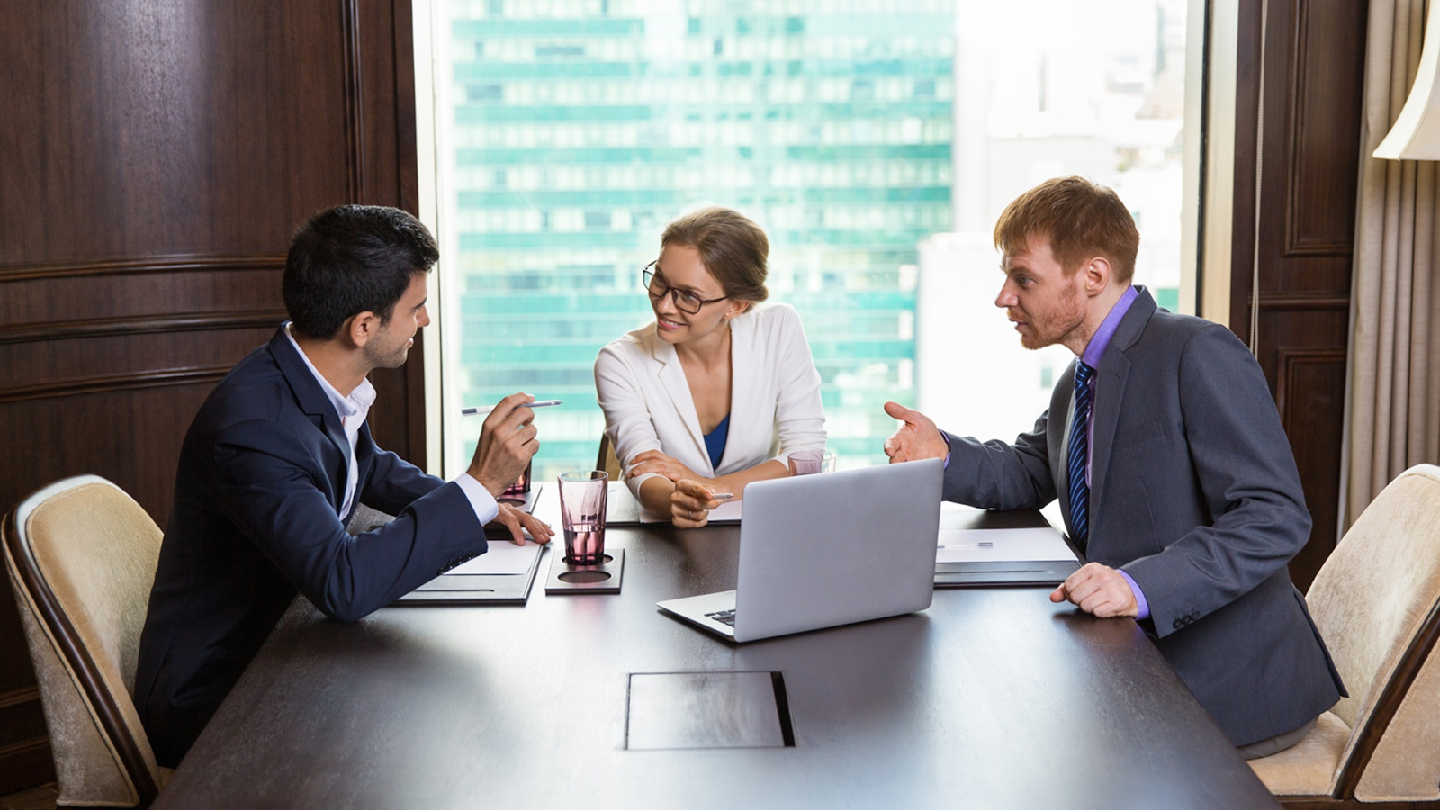 Group of business professionals discussing strategy in a conference room with city skyline view.