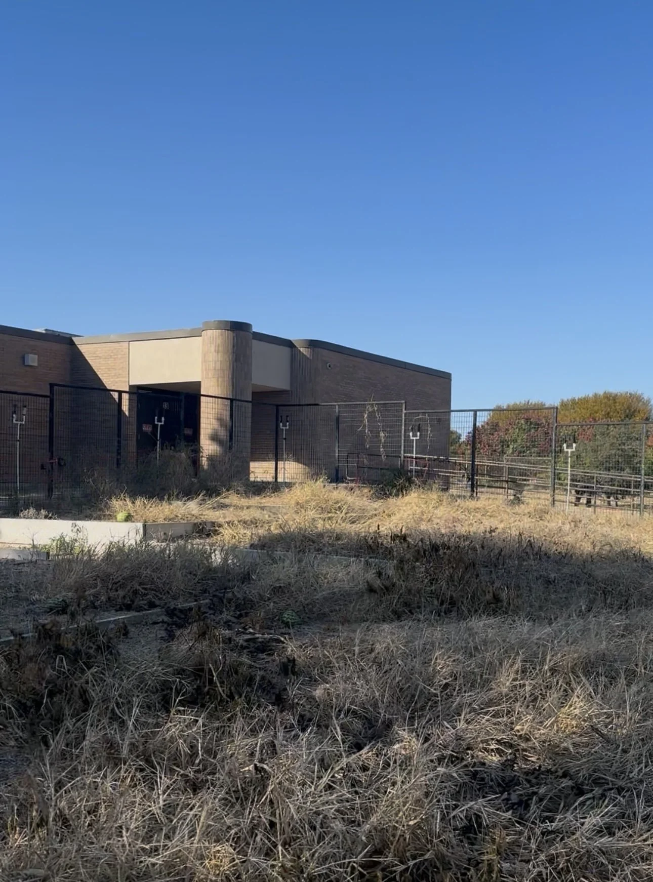An exterior view of a school building with a fenced-in yard and a clear blue sky.