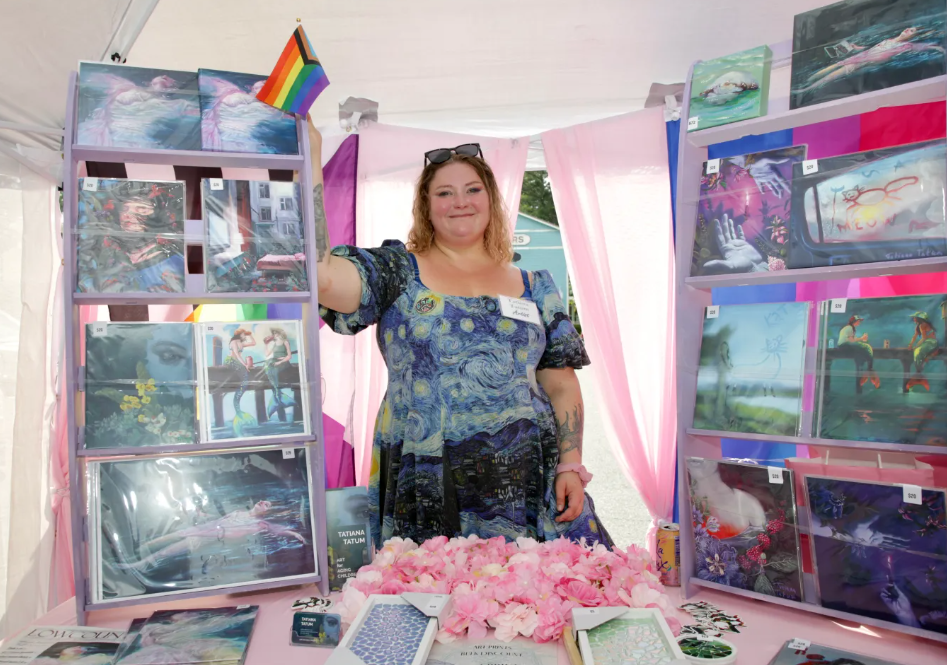 Woman standing at a booth with paintings and a pride flag