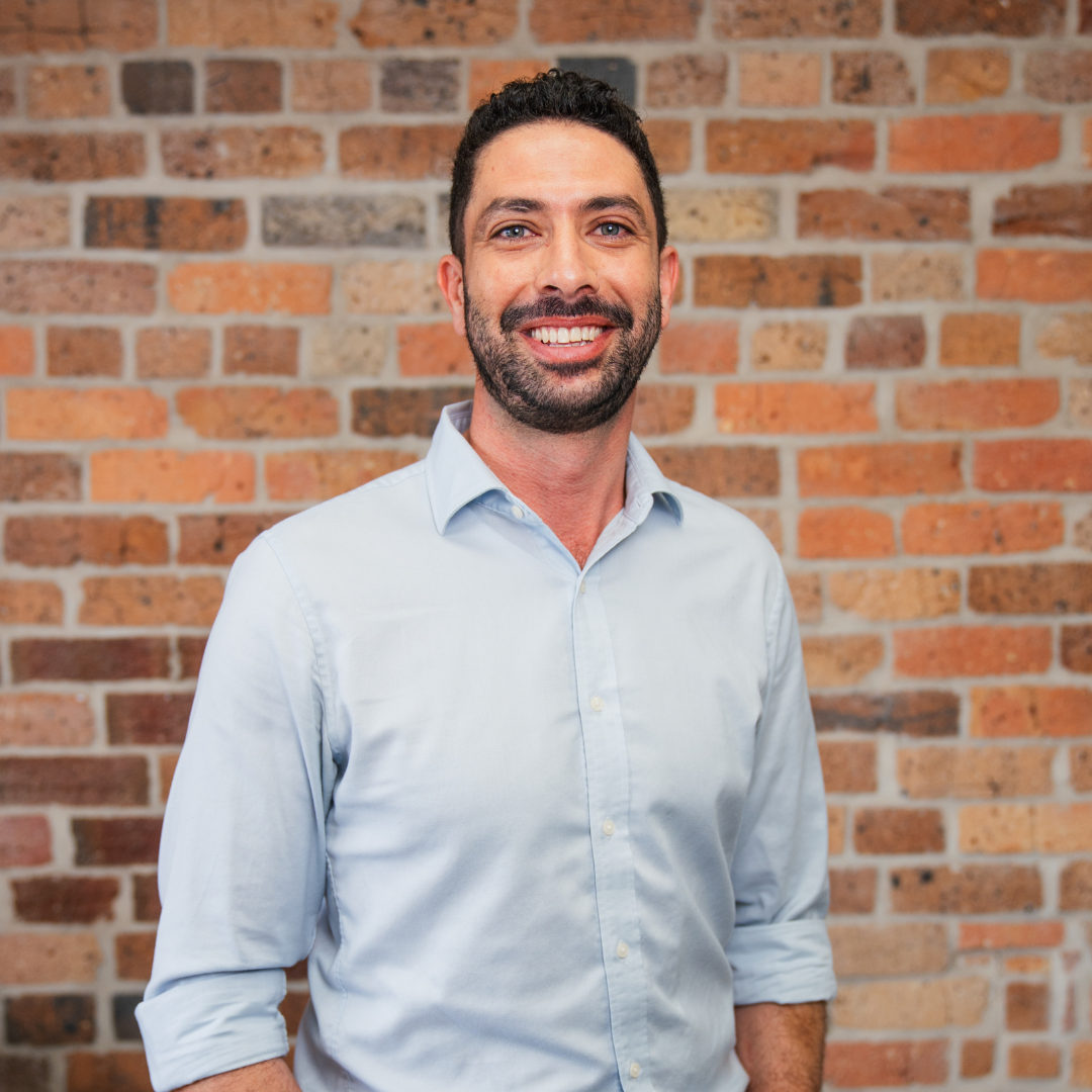 Portrait of a smiling man with dark hair and beard, wearing a suit and white shirt, in black and white.