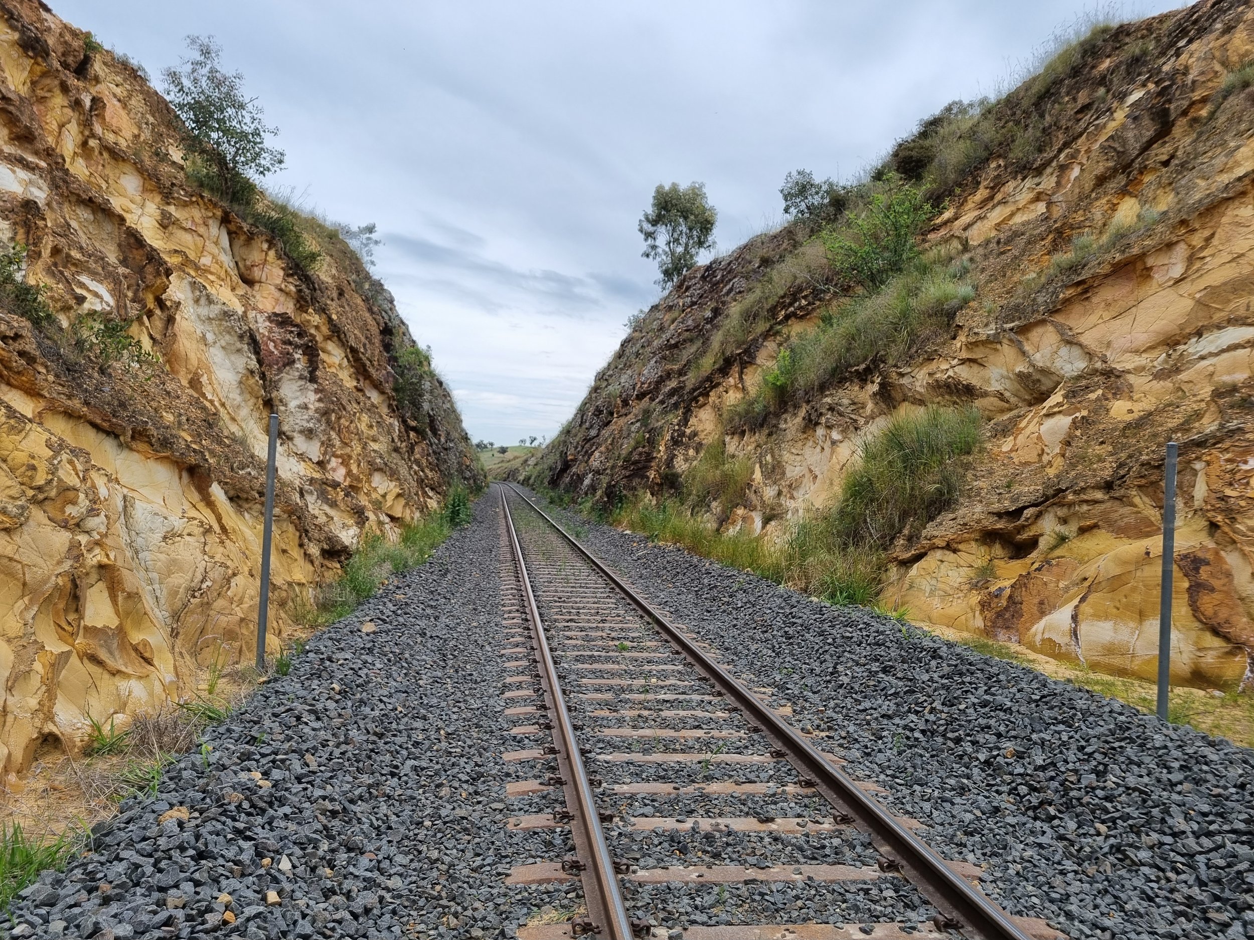 A railroad track running through a narrow pass between rocky hills under a cloudy sky.