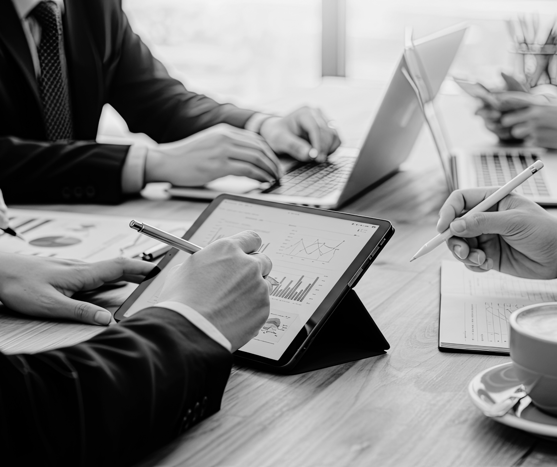 Business meeting with multiple people using electronic devices, including a tablet, laptop, and smartphones, displaying charts and graphs, in a well-lit office setting.