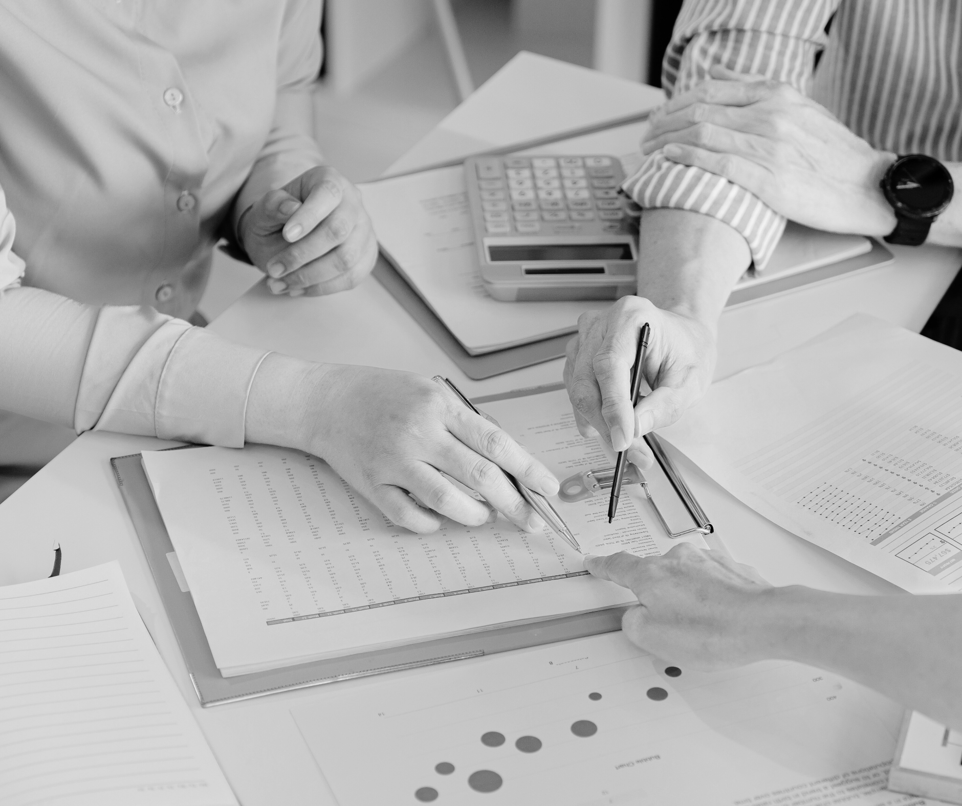People working on financial paperwork at a desk, with documents, notebooks, and a calculator.