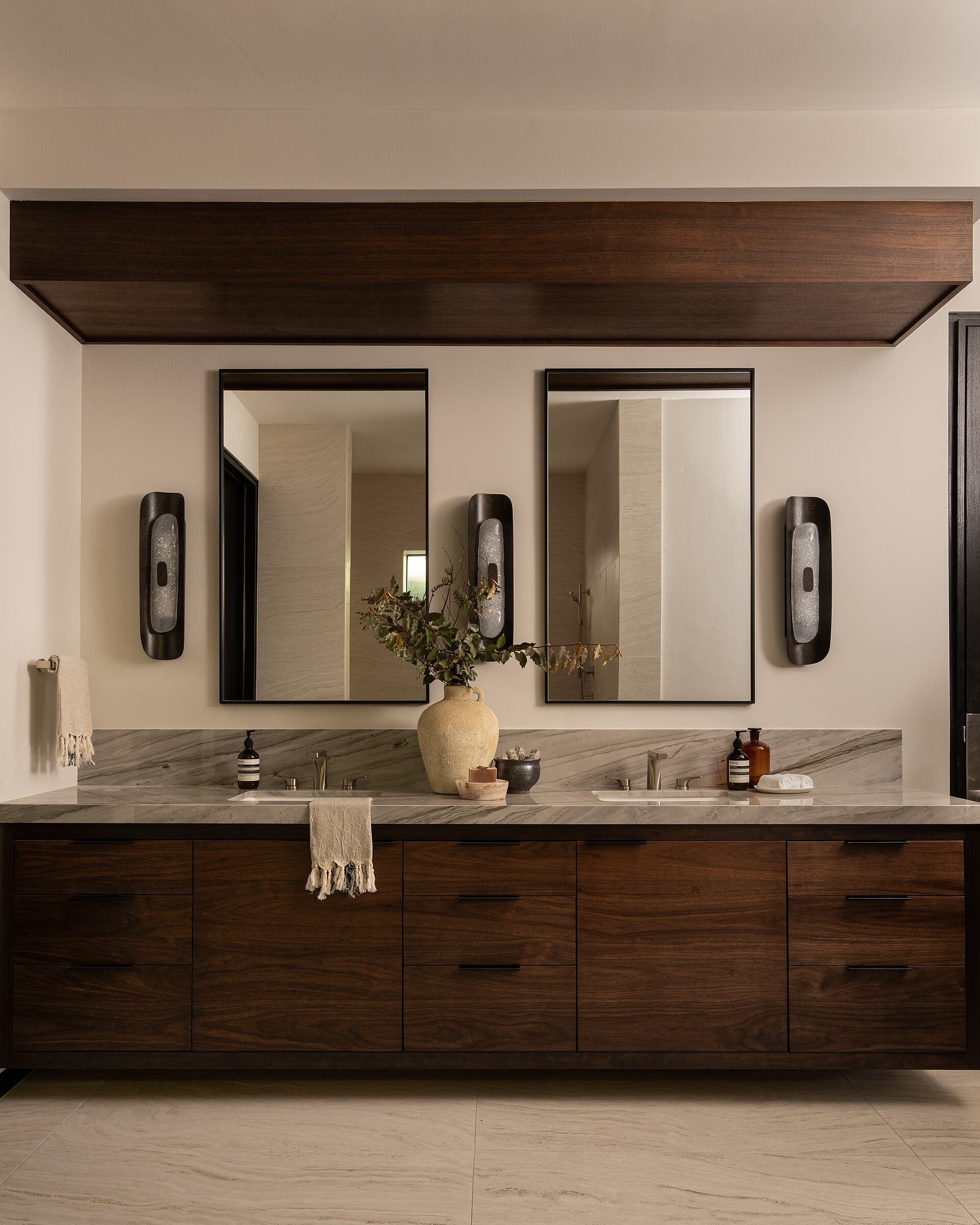 Paired mirrors and carved stone sconces above a walnut double vanity