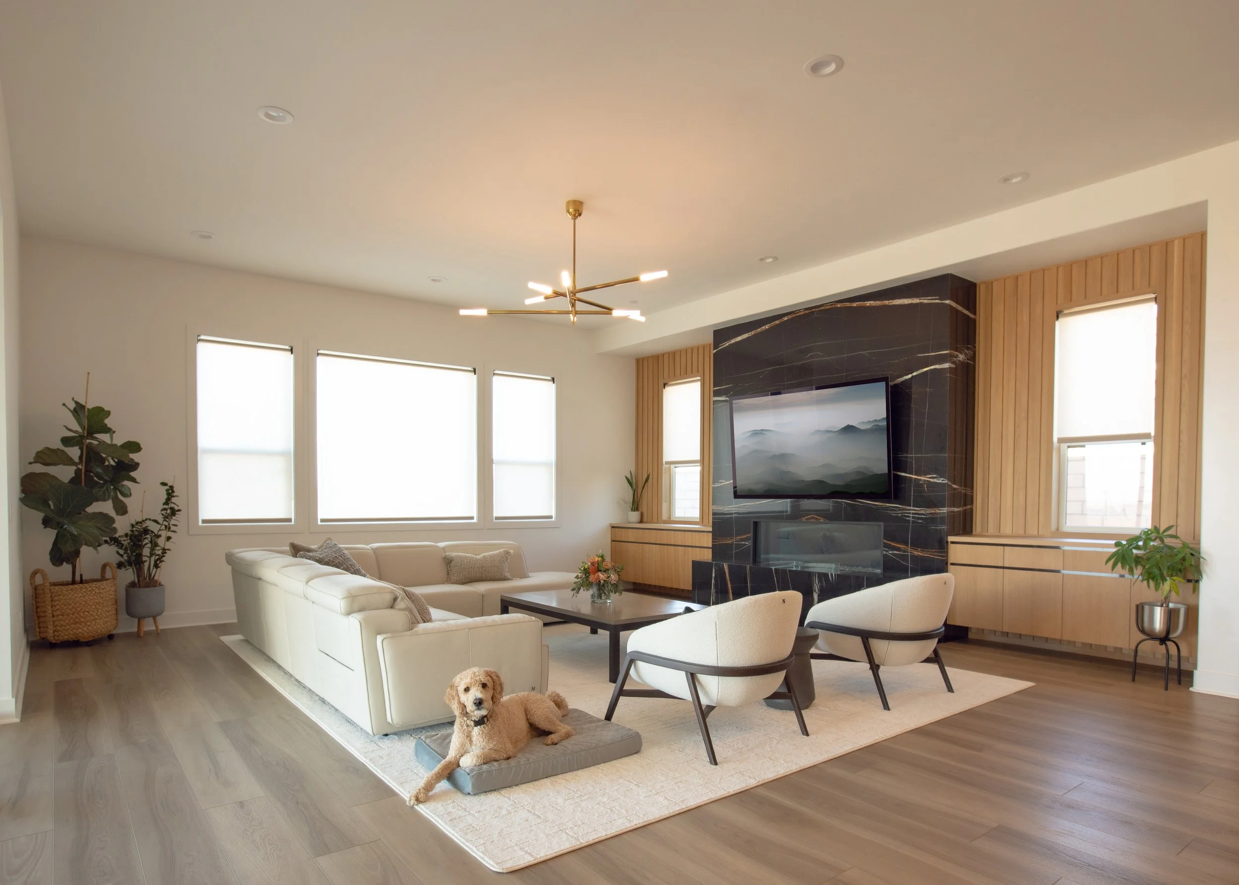 warm great room black marble stone fireplace white oak vertical slat wall floating cabinets modern clean lined sectional and curved upholstered chairs gold chandelier 