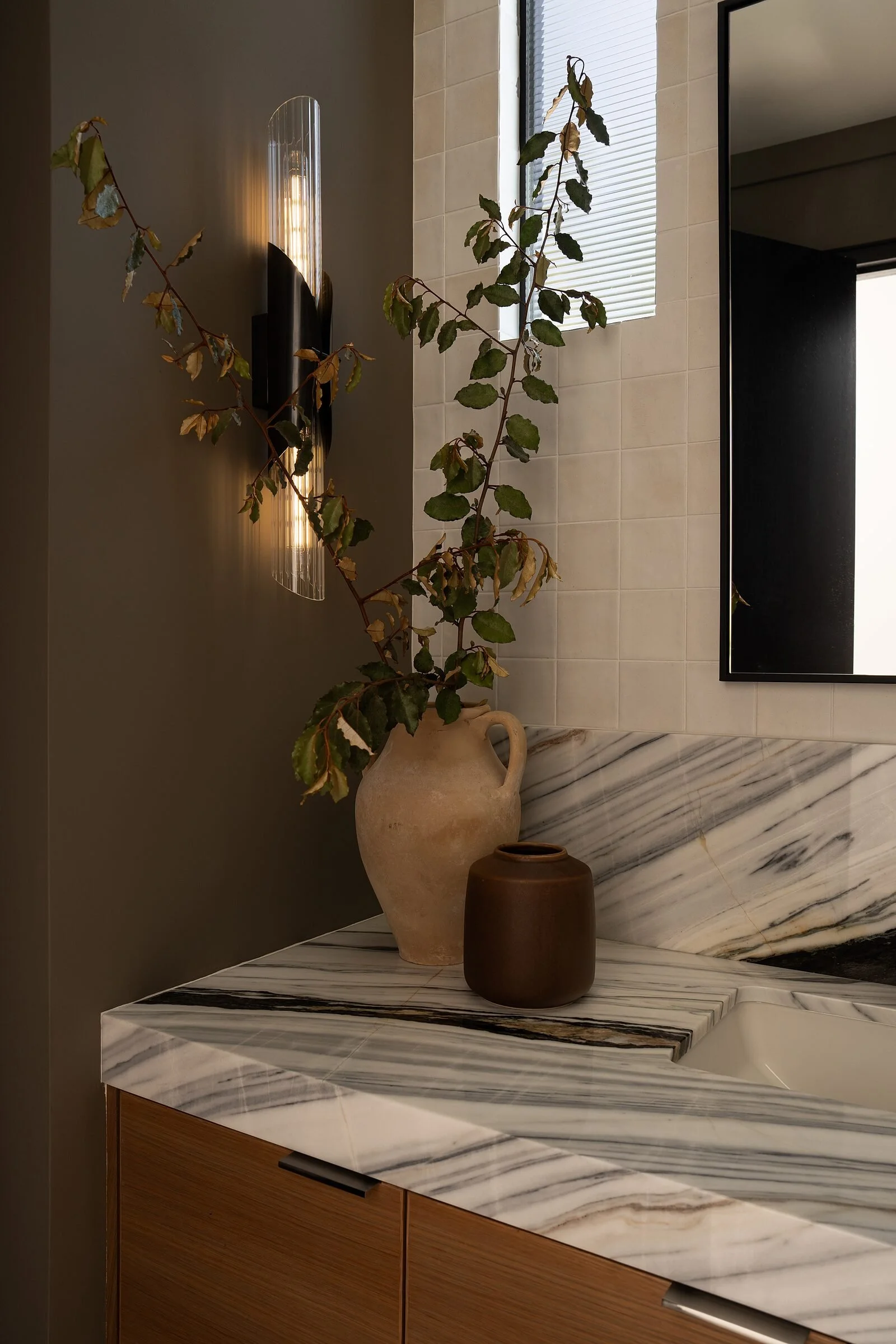 Glass sconce and ceramic vessels on a stone powder room counter
