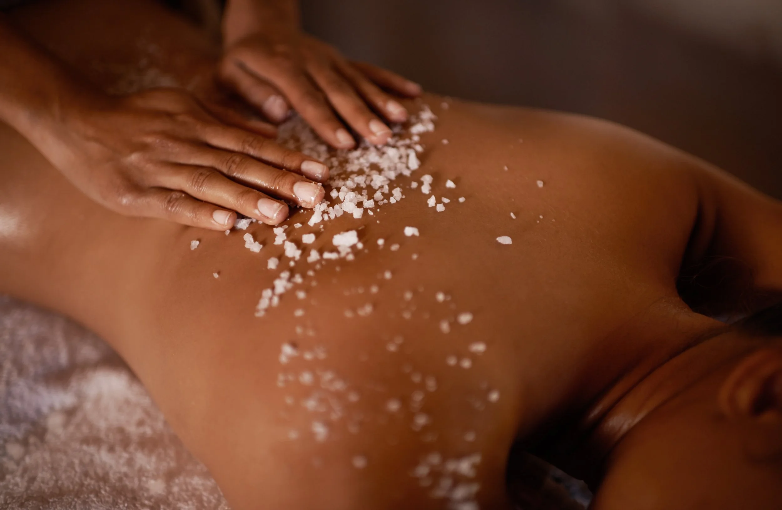 Person receiving a body scrub massage, lying face down with salt being sprinkled on their back.