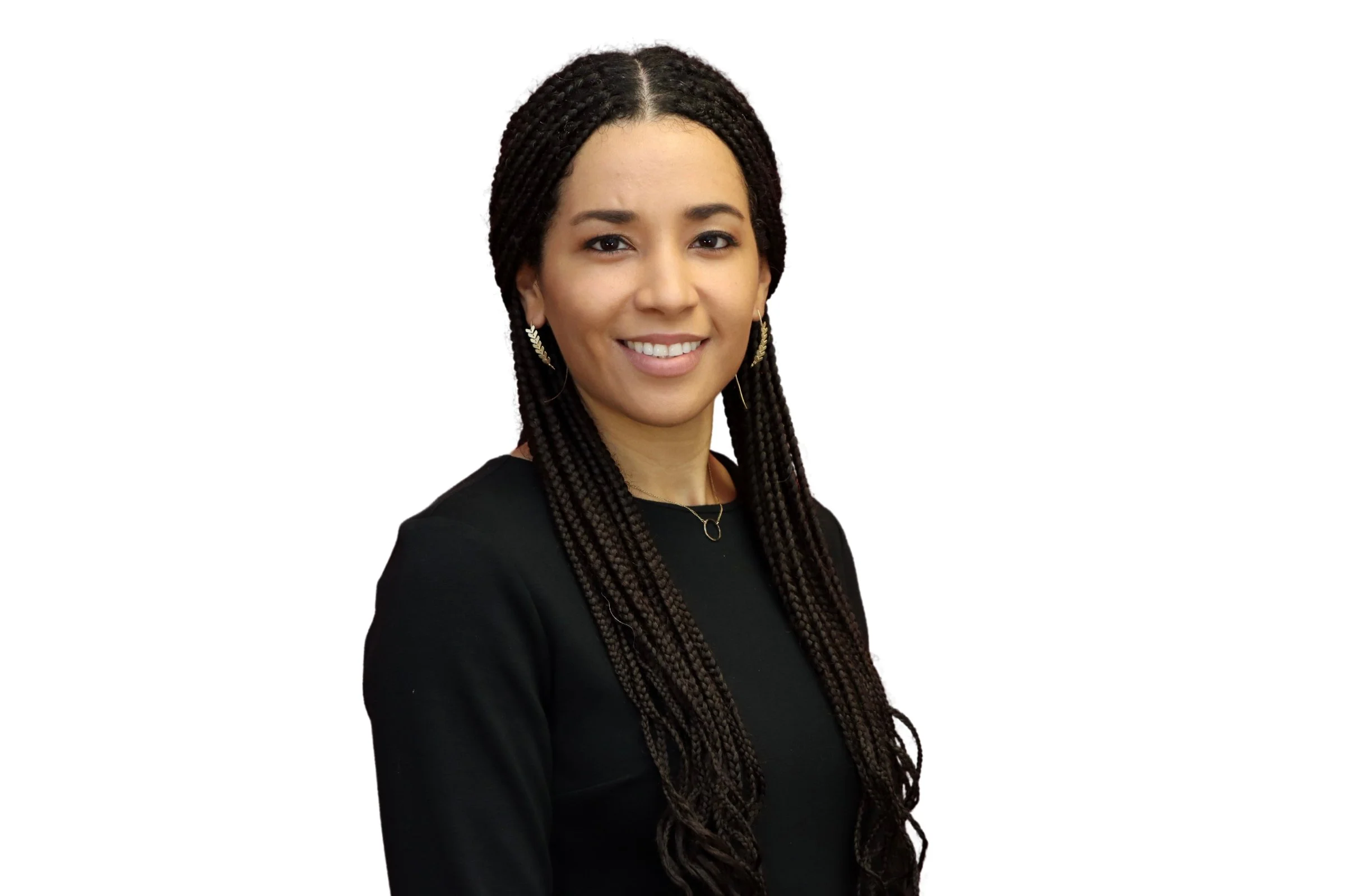 Portrait of a young woman with long braided hair, wearing a black dress, earrings, and a necklace, smiling against a white background.