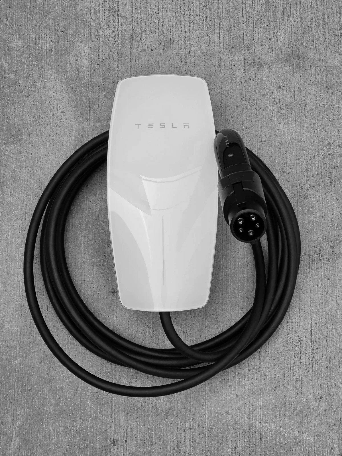 Tesla electric vehicle charging station with a black charging cable and connector on a concrete surface.