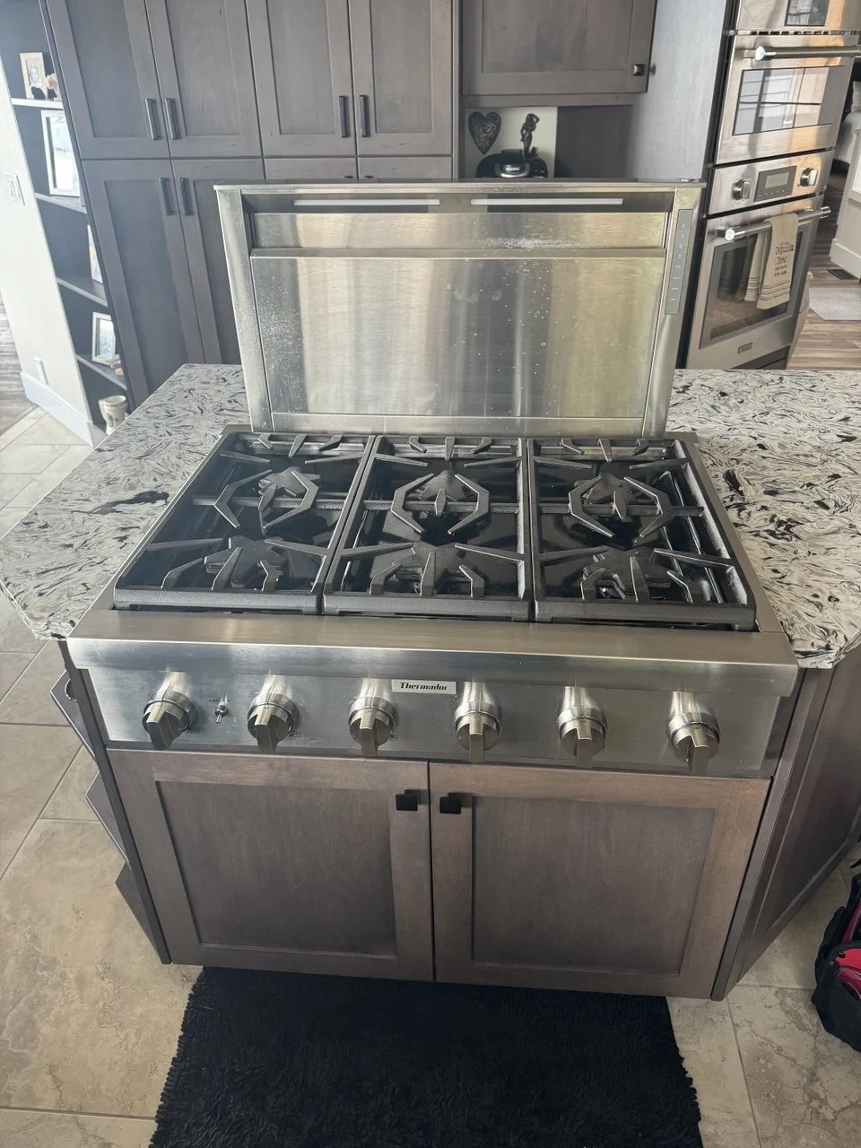Stainless steel gas range with four burners in a kitchen with gray cabinets and granite countertops.