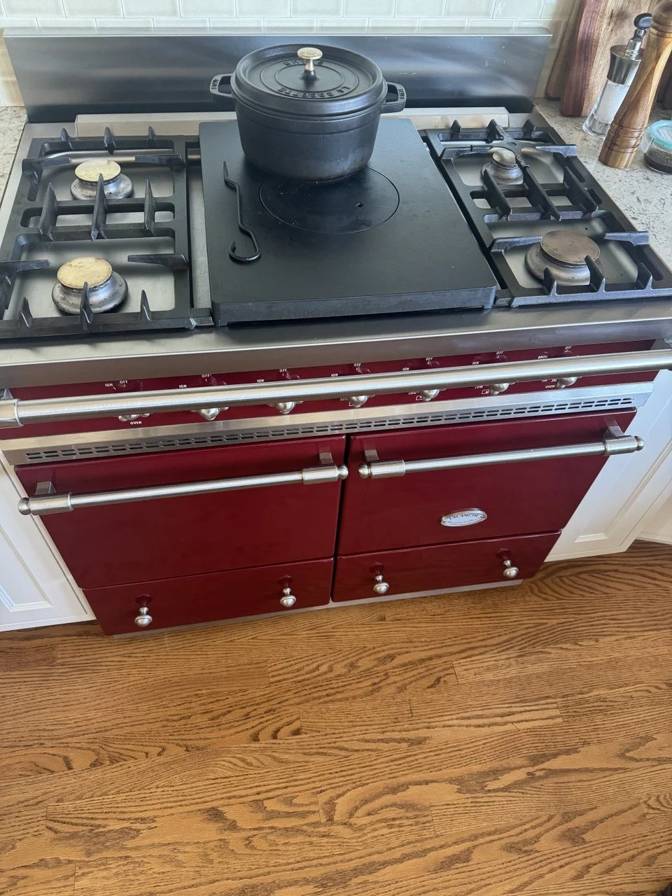 Red vintage gas stove with four burners, a black pot on the middle burner, and a wooden floor in front.