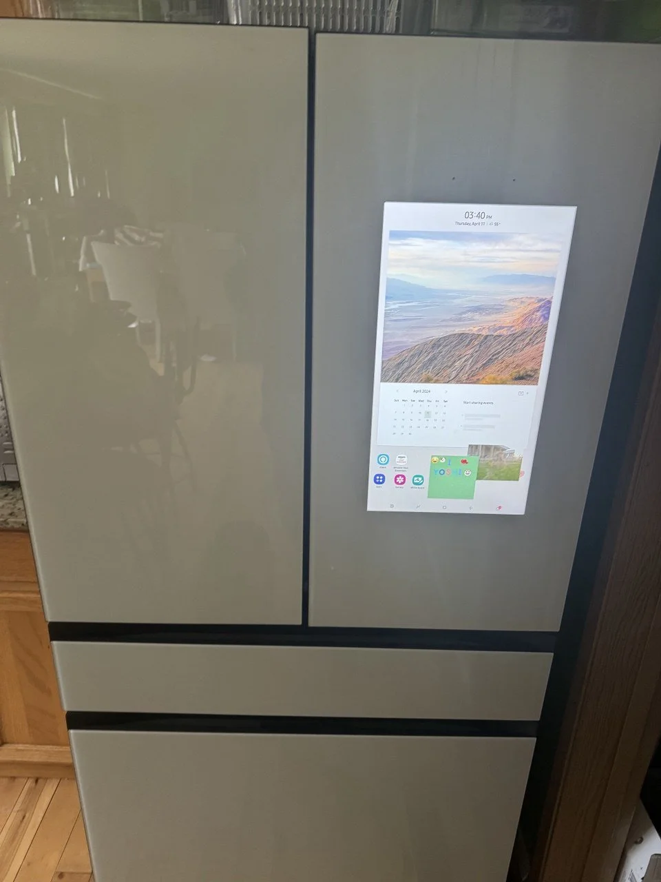 A refrigerator with a built-in digital screen displaying the time, date, calendar, and app icons.