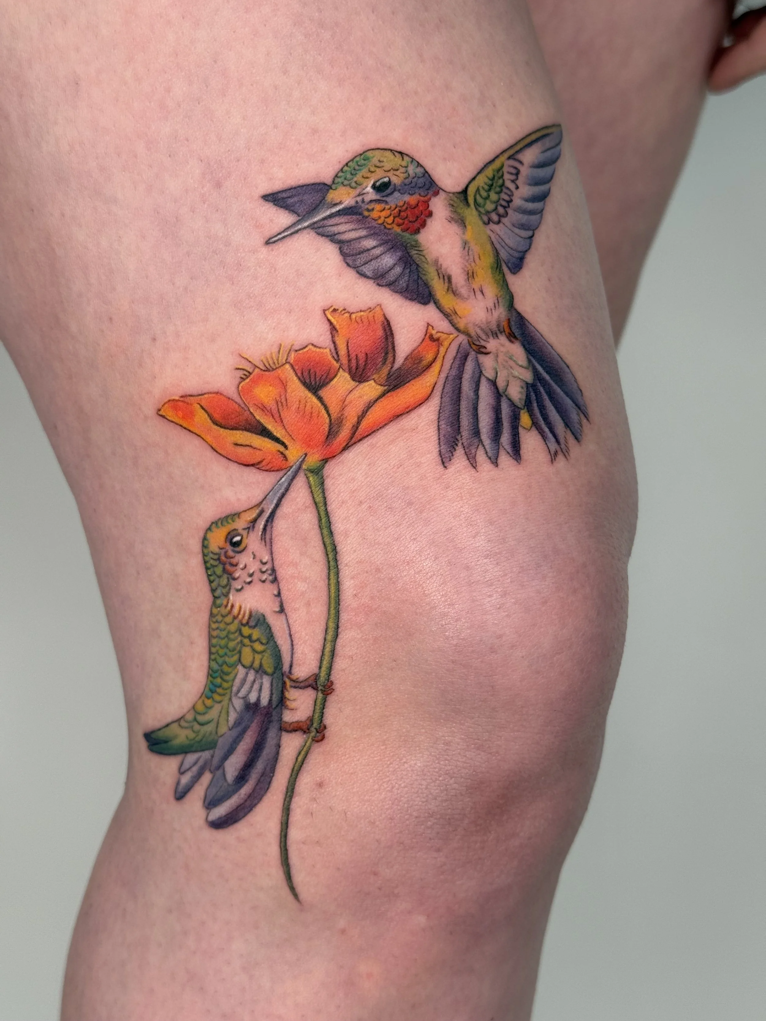 Colorful tattoo of two hummingbirds and orange flowers on skin.