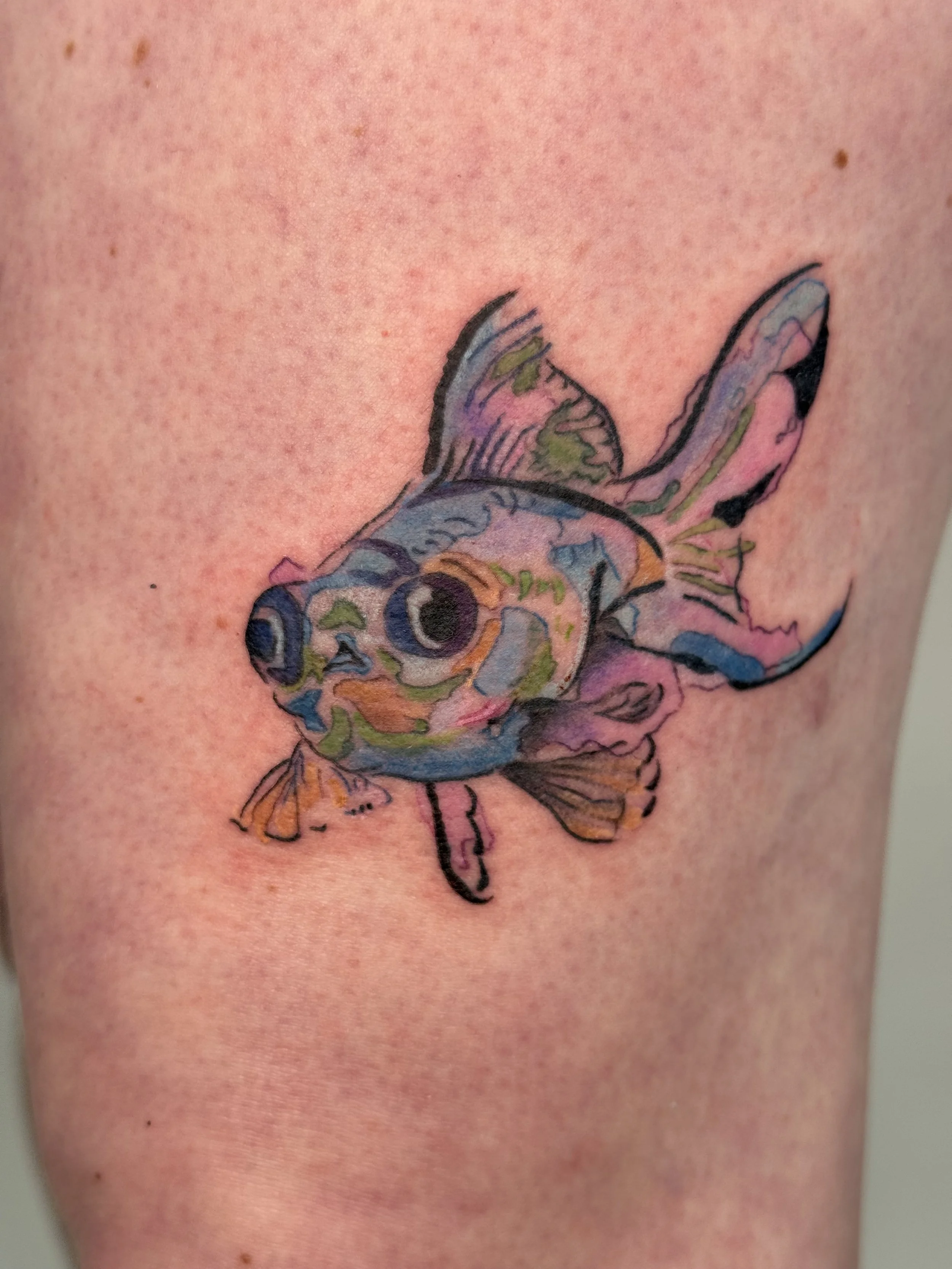 Colorful tattoo of a fish with large eyes on skin.