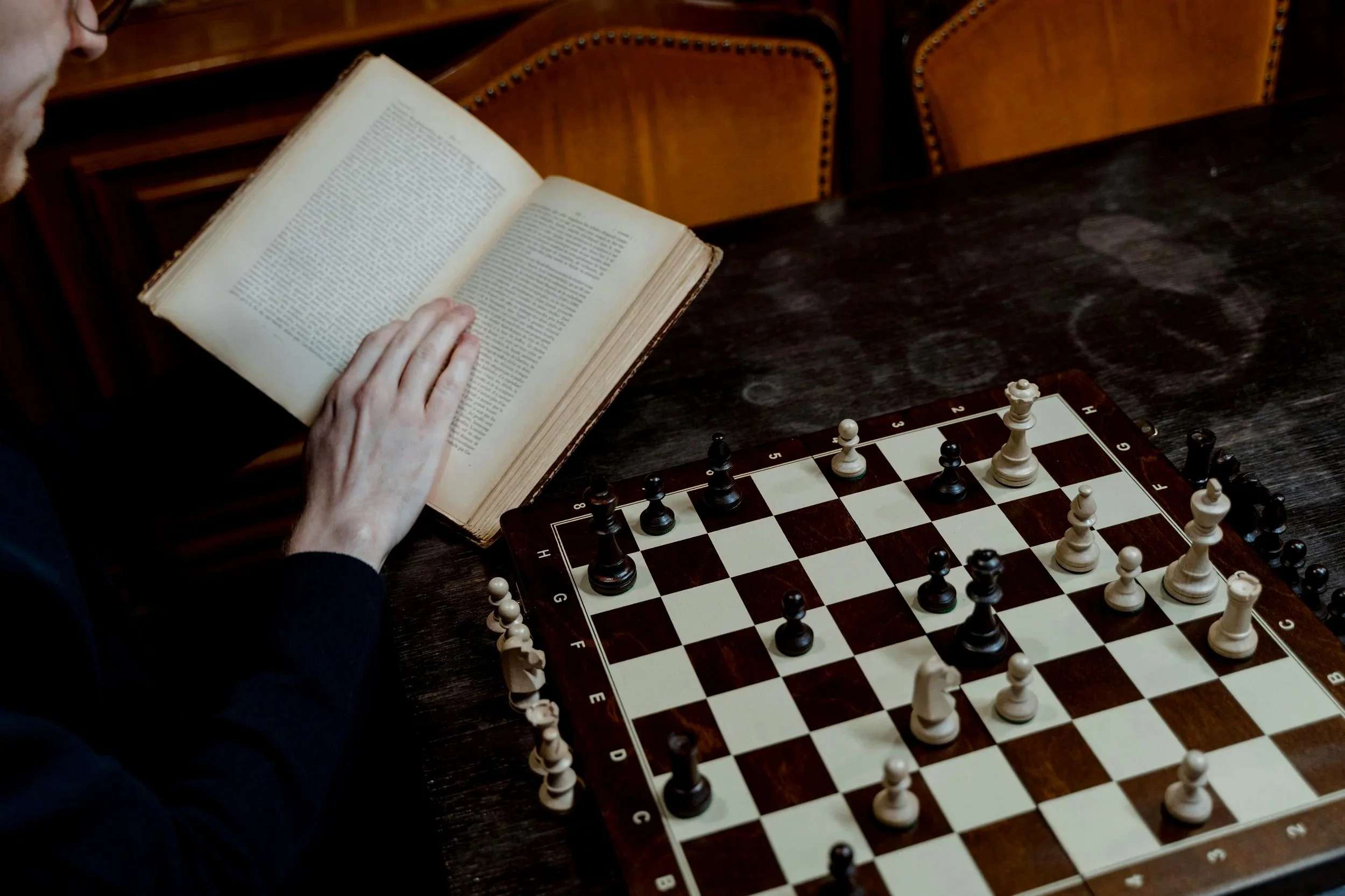 Person reading a book at a table with a chessboard.