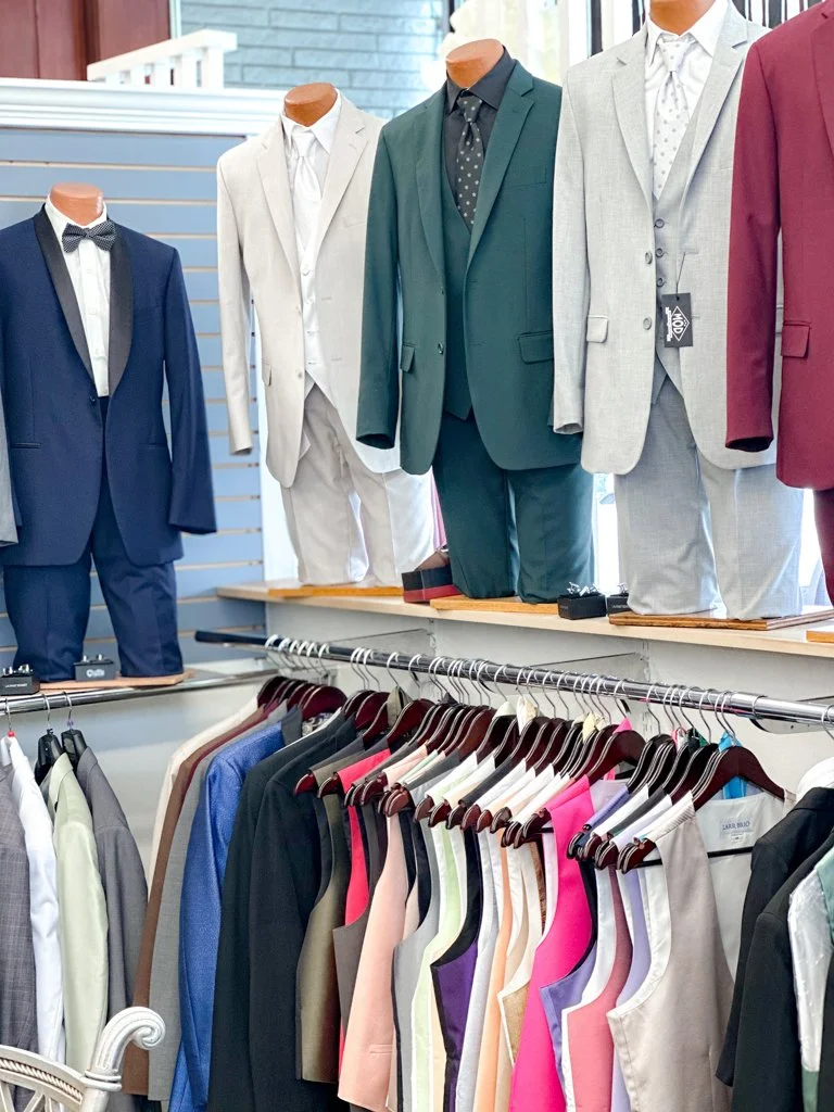 Display of men's suits on mannequins and women's tops on hangers in a clothing store