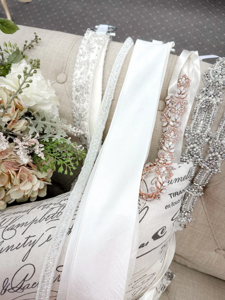 Elegant wedding accessories including pearl and rhinestone jewelry, ribbons, and a bouquet of white and blush flowers with greenery.