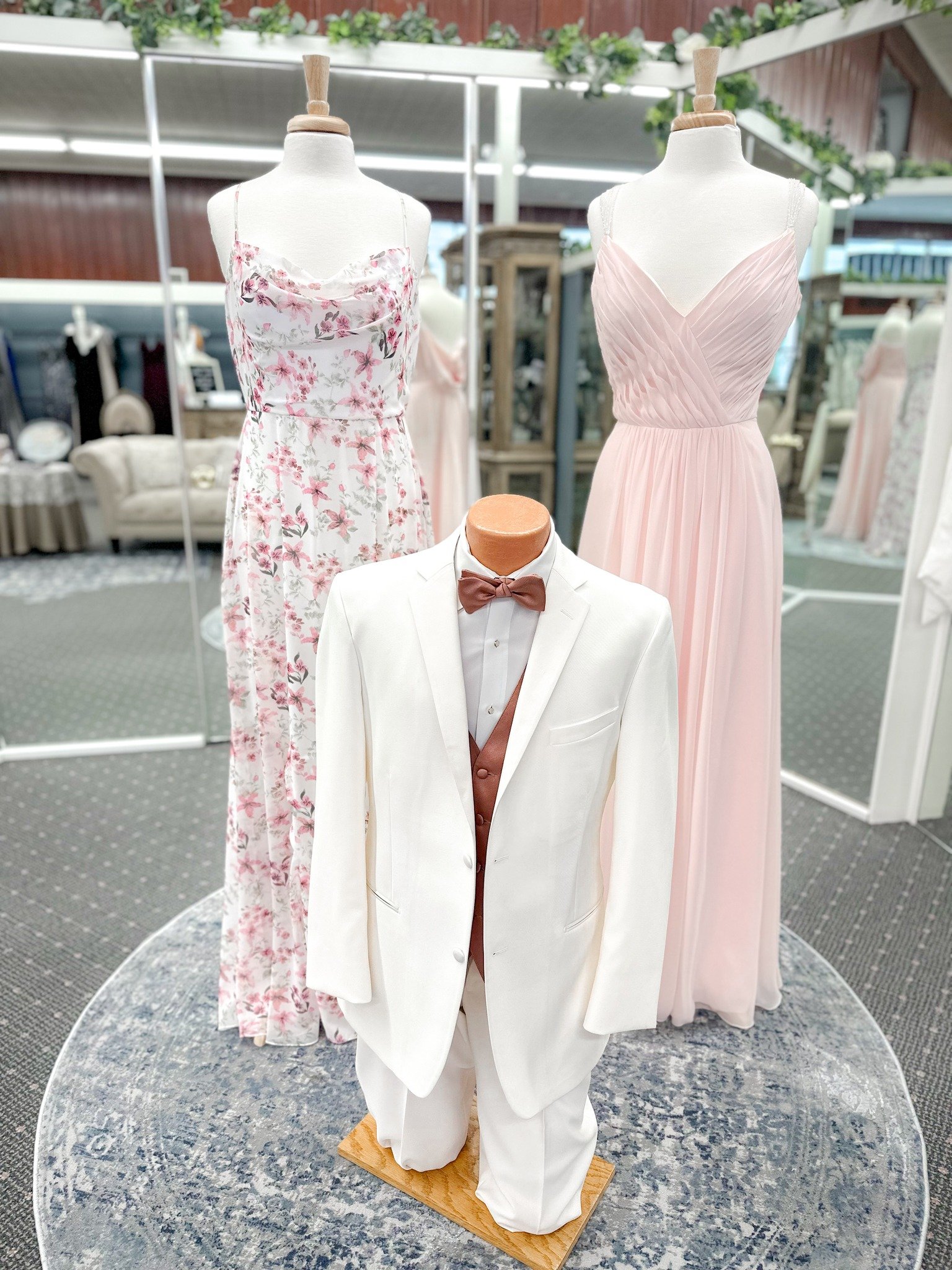 Display of formal wear including two long dresses and a tuxedo, on mannequins at a store or boutique.