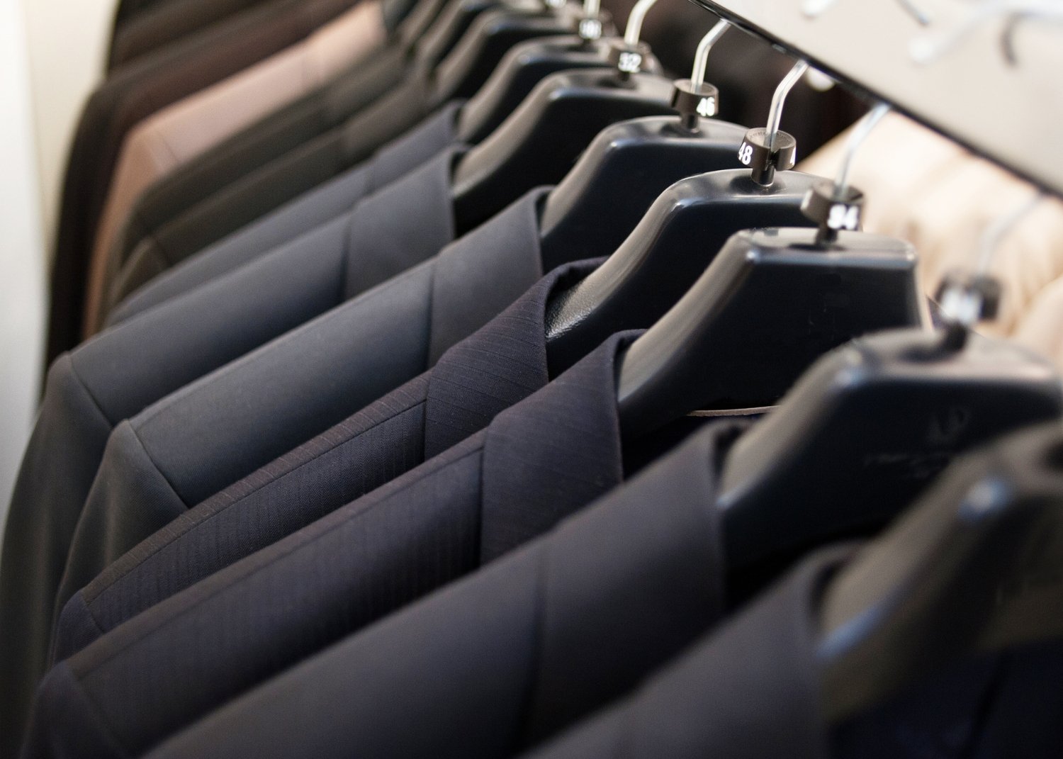 Clothes such as suits and jackets hanging on black hangers in a closet.