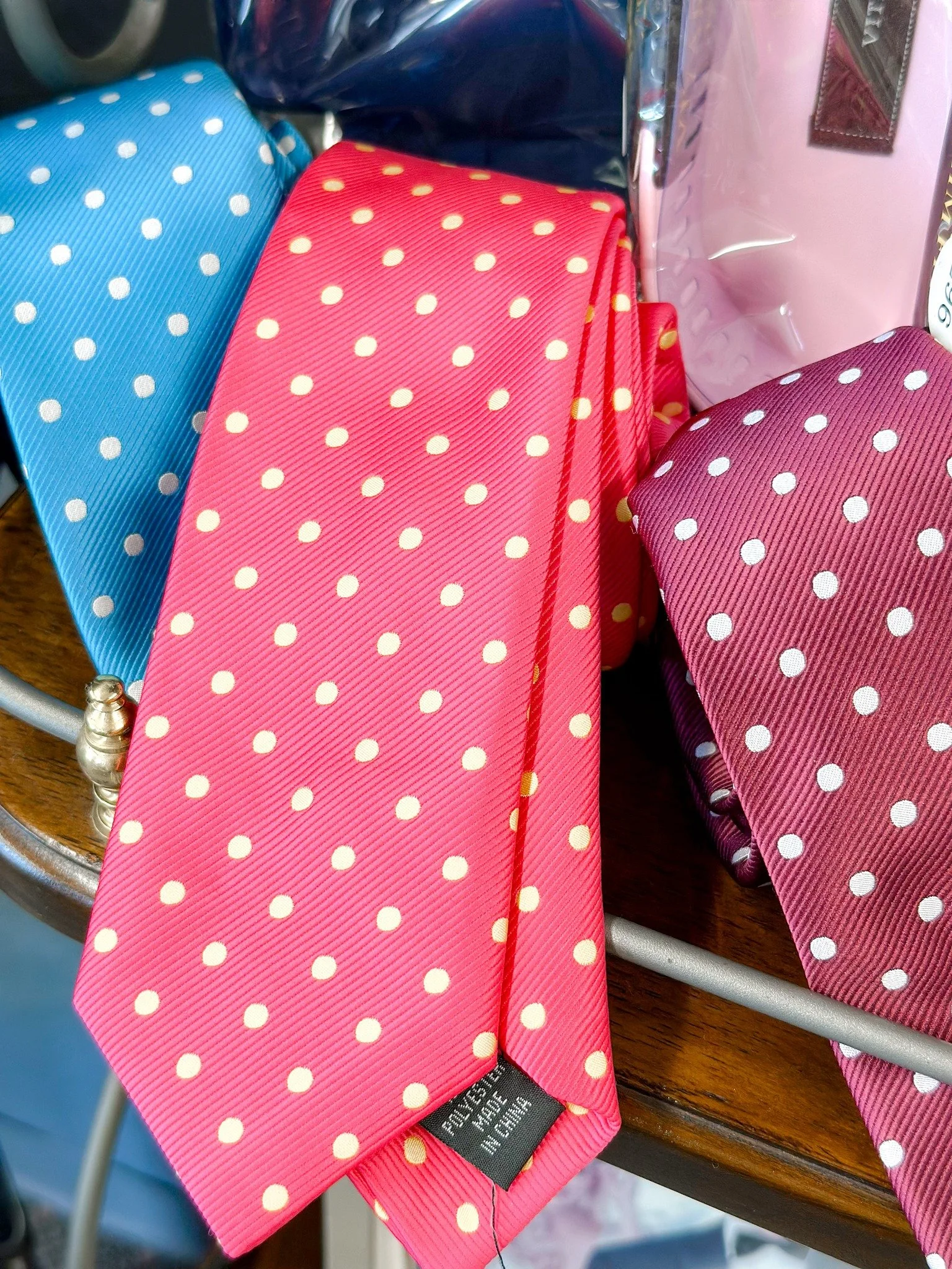 Three colorful neckties with polka dot patterns hanging on a wooden surface, featuring pink, purple, and blue colors.