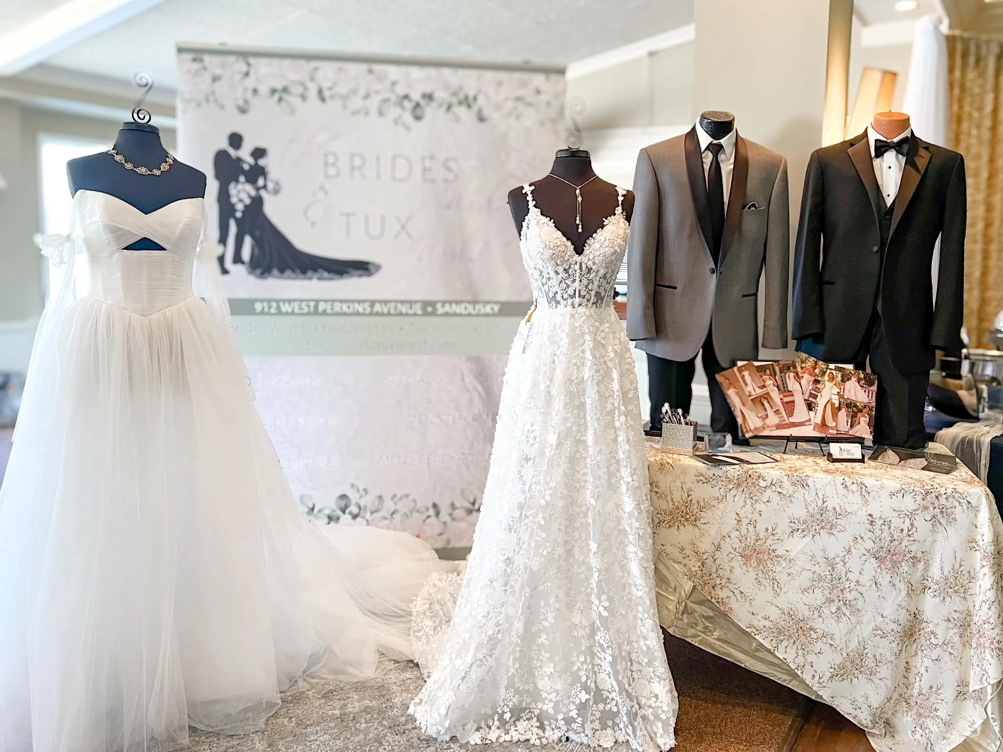 Display of bridal and groom fashion at a wedding boutique, featuring wedding dresses on mannequins and tuxedos on mannequins, with a signage in the background