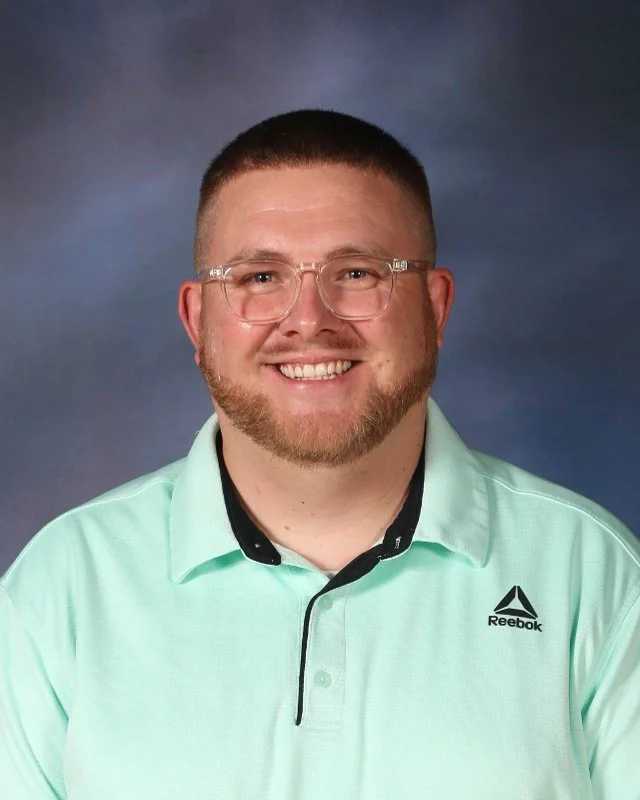 Portrait of a smiling man with short hair and glasses, wearing a light green Reebok polo shirt, against a dark blue gradient background.