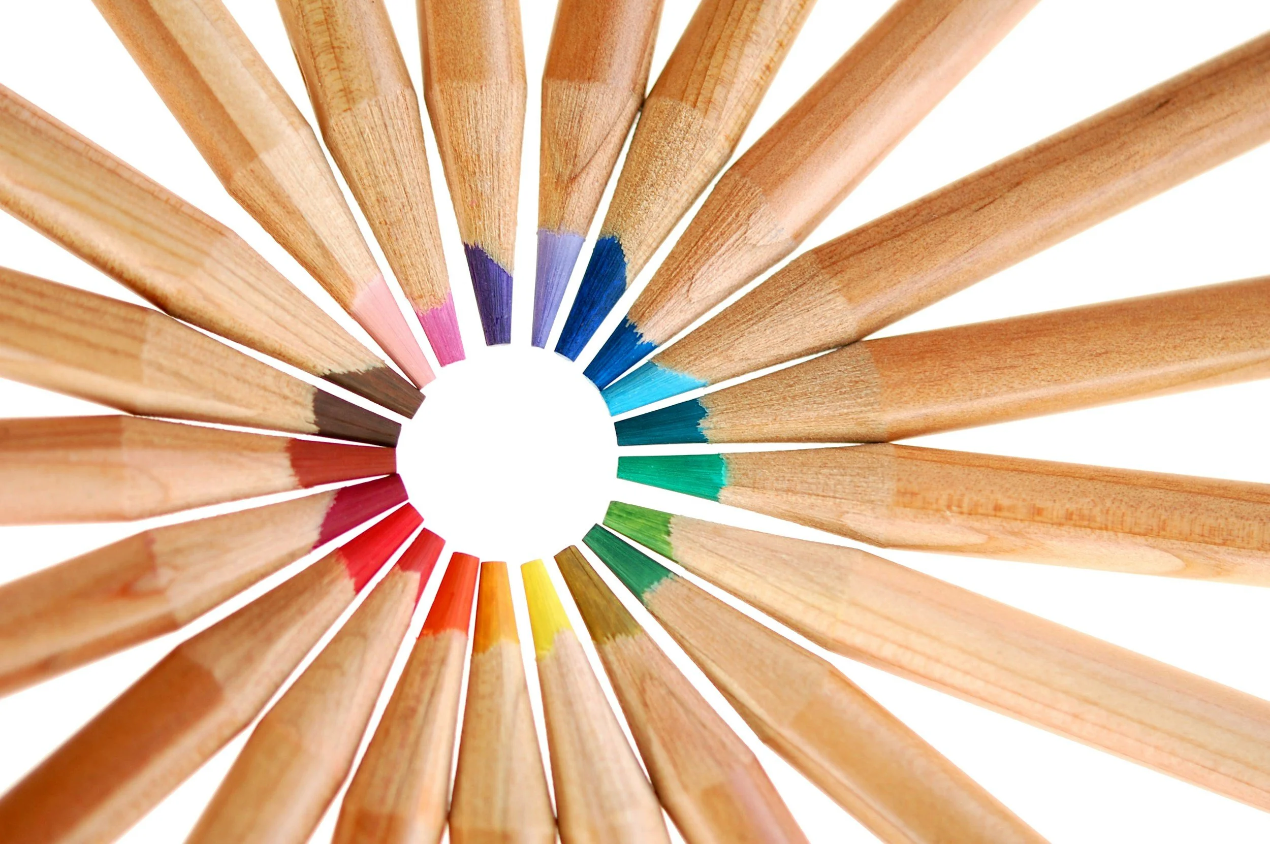 Colored pencils arranged in a circle, with tips pointing toward the center, showcasing a spectrum of colors from pink to dark blue to green and yellow.