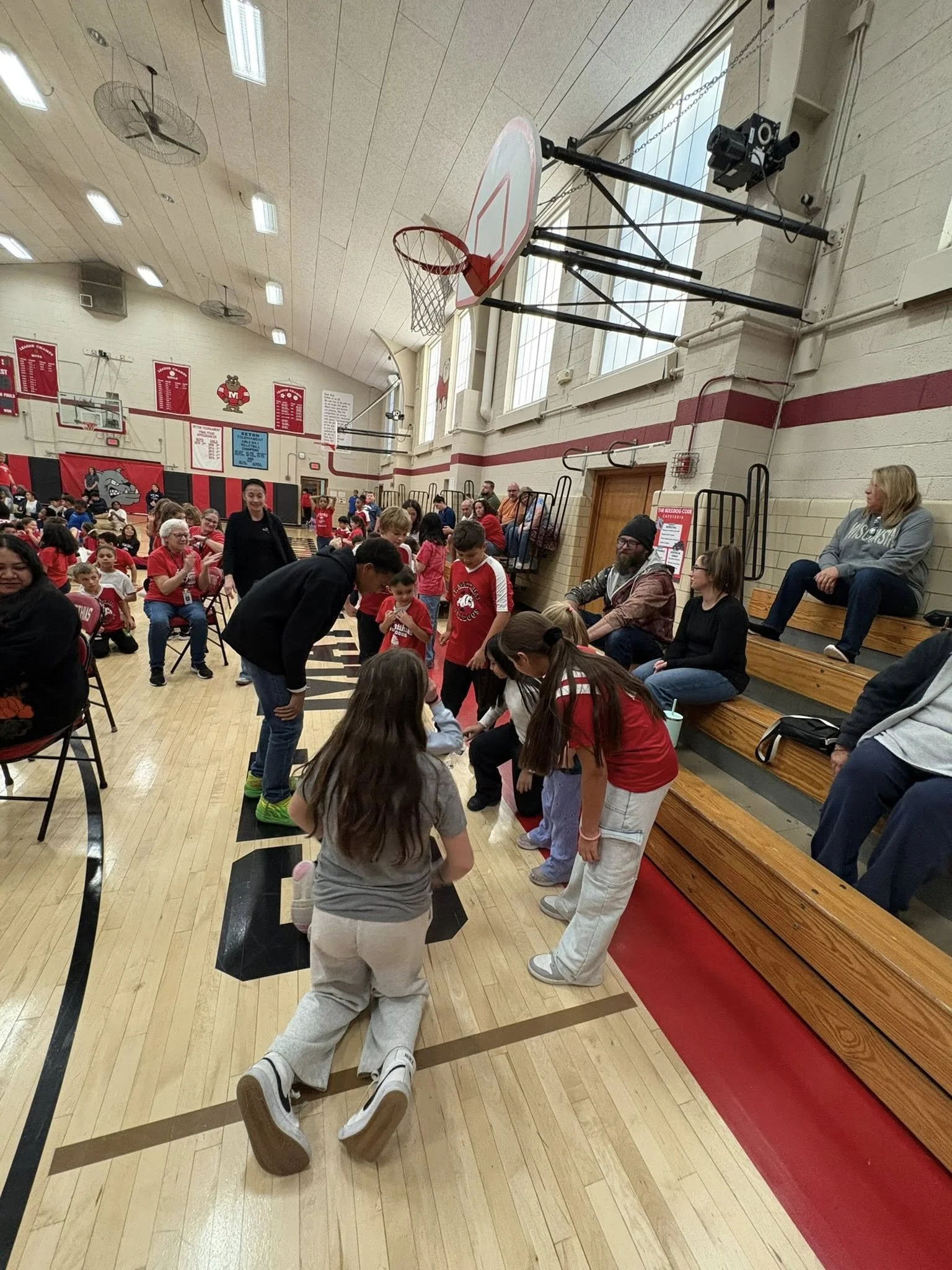 Children and adults participating in a game or activity inside a gymnasium decorated in the school's red and black colors, celebrating the success of the Catholic School Sole Walk.