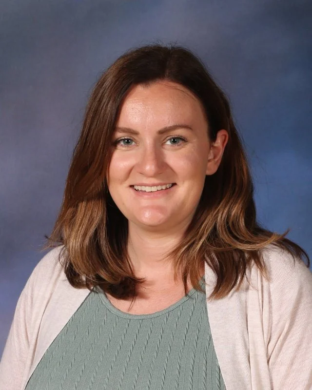 Portrait of a smiling woman with shoulder-length brown hair, wearing a green top and beige cardigan, against a blue gradient background.