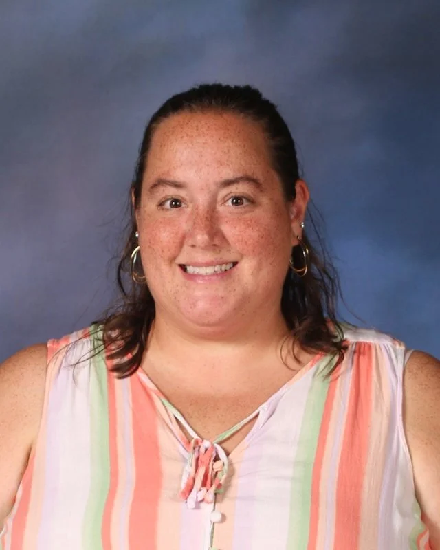 A woman with brown hair pulled back, wearing hoop earrings and a sleeveless top with pastel vertical stripes, smiling against a blue background.