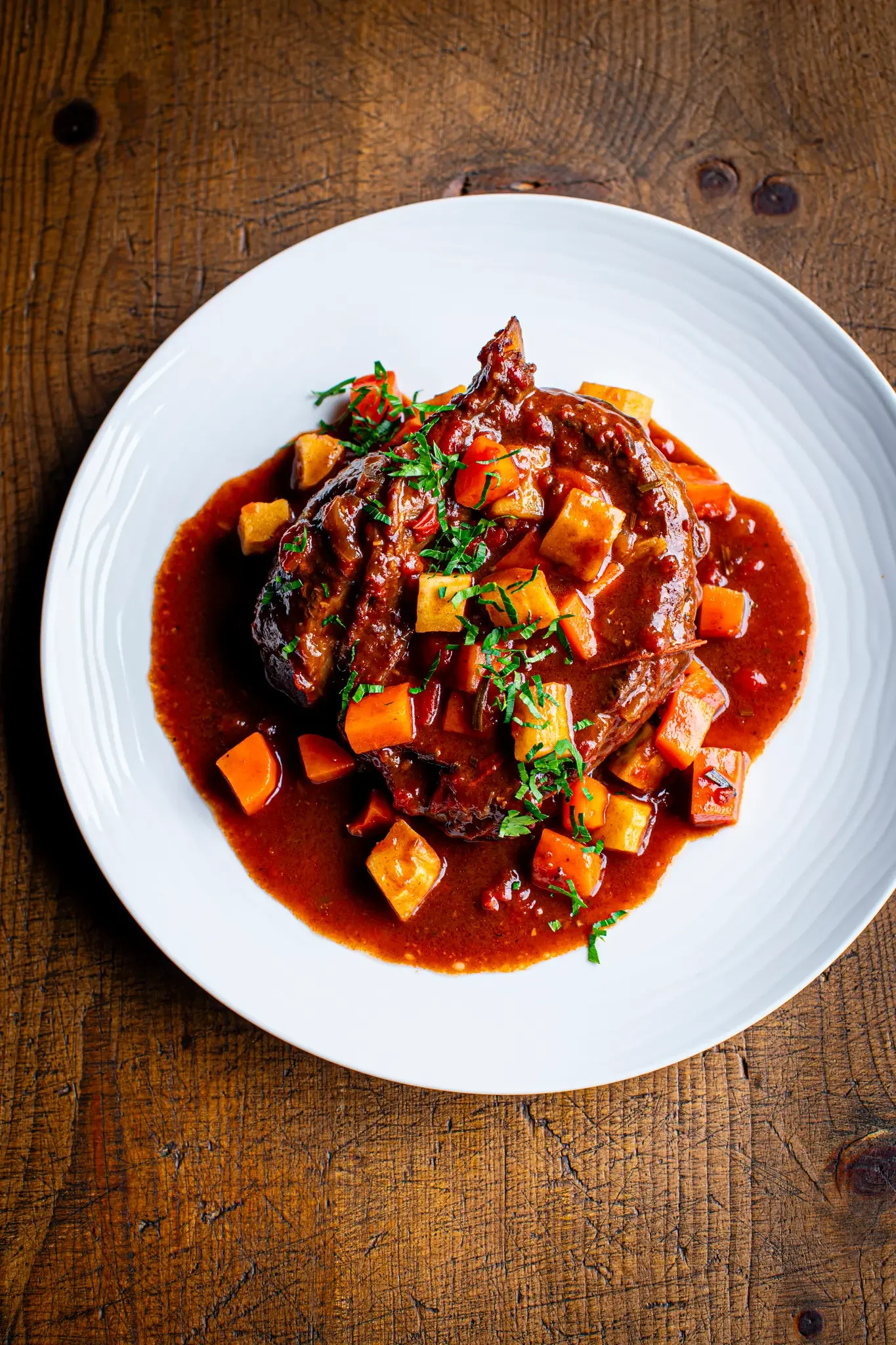 A plate of beef stew with carrots, potatoes, and herbs, served with a rich, dark sauce.