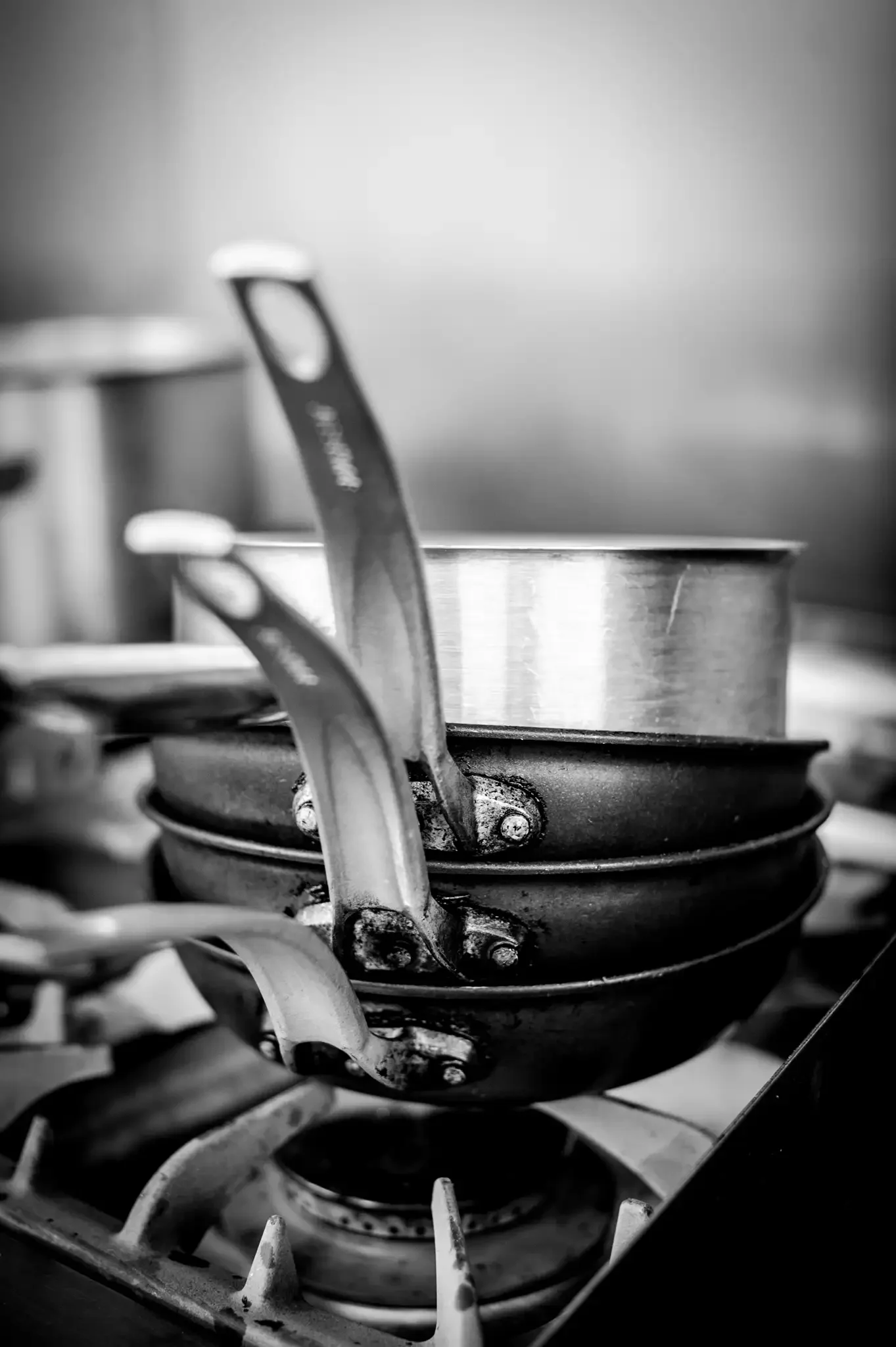 Close-up of stacked pots and pans on a stovetop burner, black and white photograph.