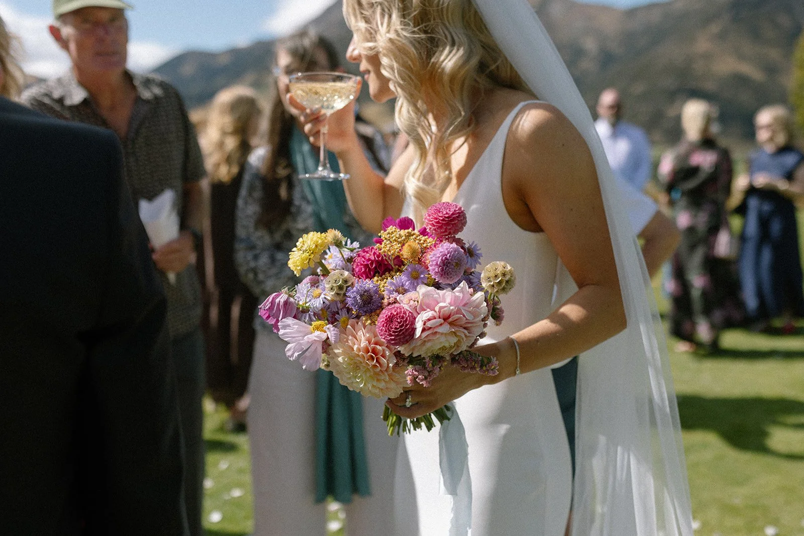 A bride holding a colorful bouquet of flowers at an outdoor wedding ceremony.