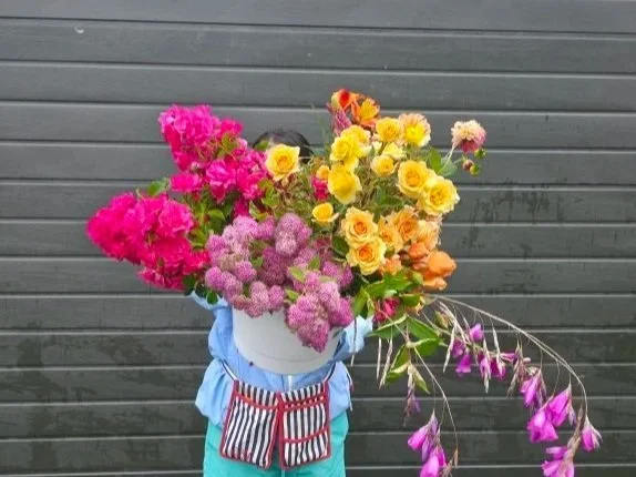 A person holding a large bouquet of colorful flowers in front of a gray wooden wall.