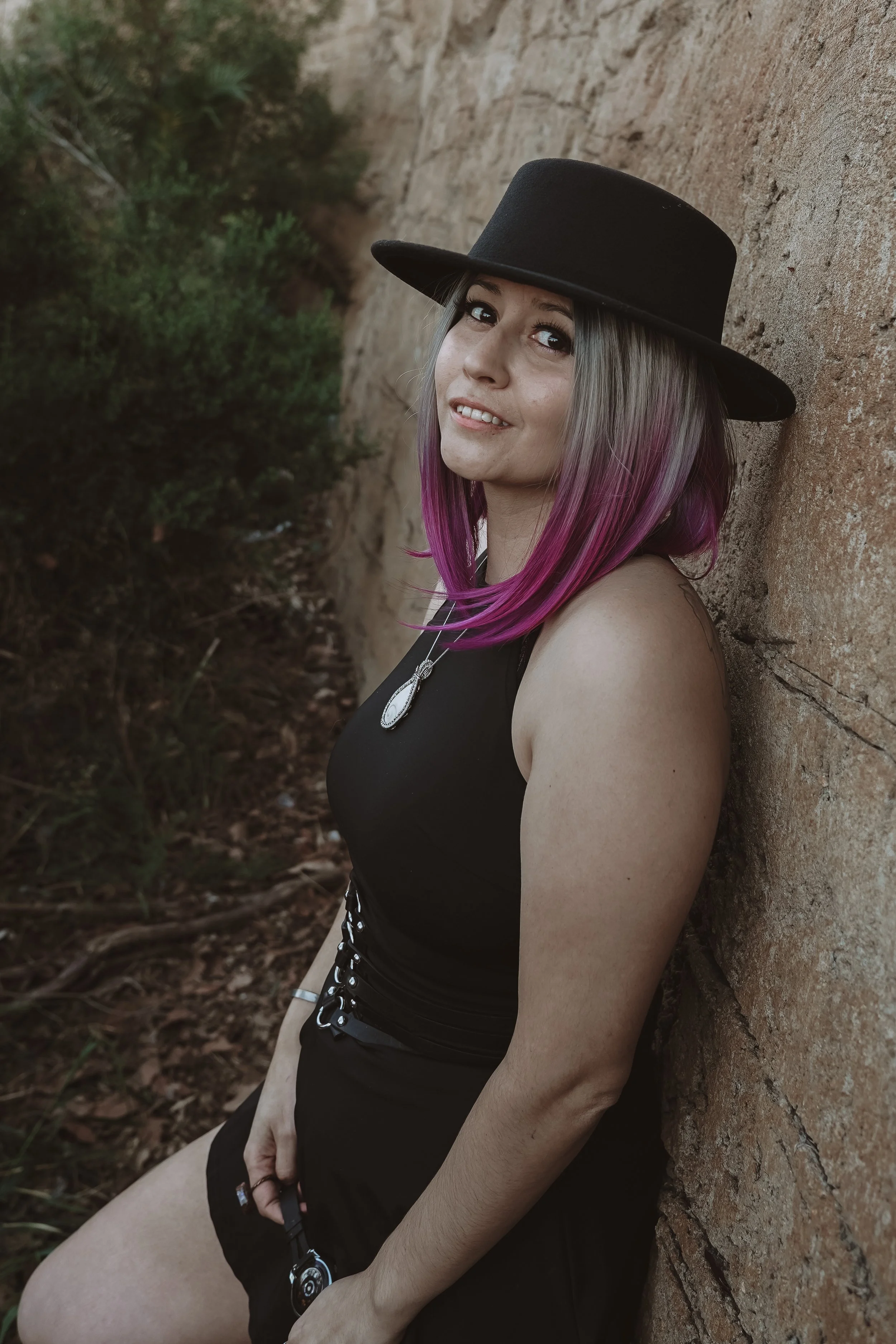 Environmental portrait of Sirona Faeryn outdoors against a stone wall, photographed by Rom Faeryn.