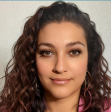 A young woman with shoulder-length black hair smiling in a lush, green indoor garden.